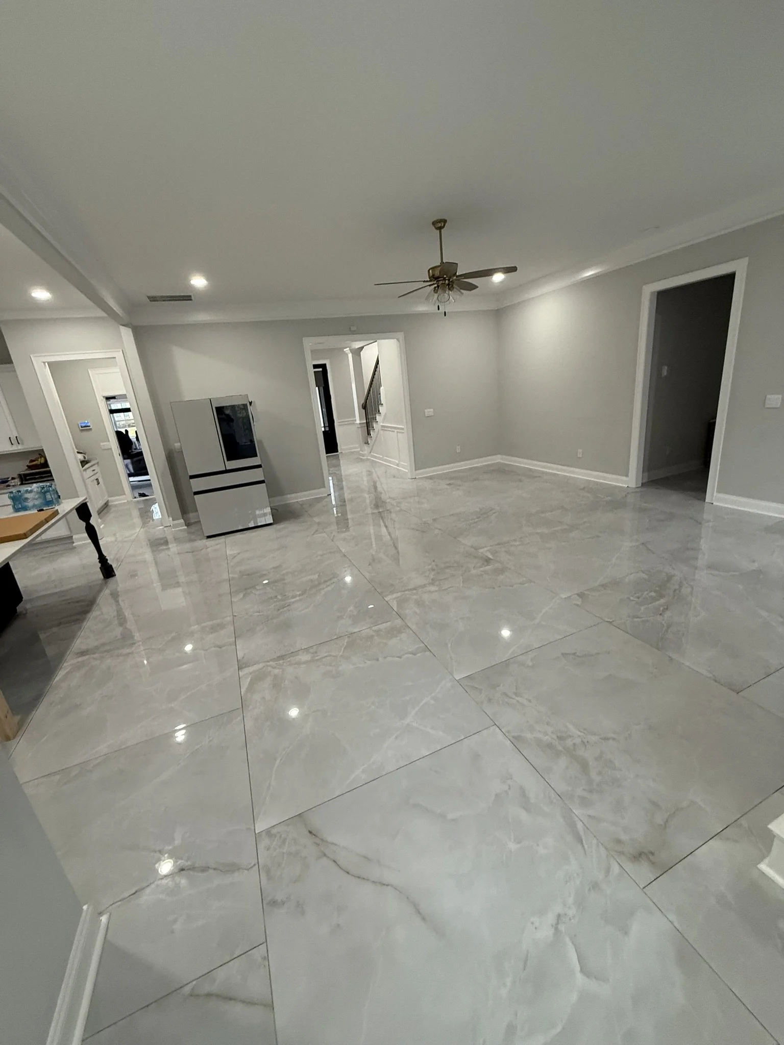 Empty living room with large marble floor tiles, gray walls, a ceiling fan, and open doorways to other rooms.