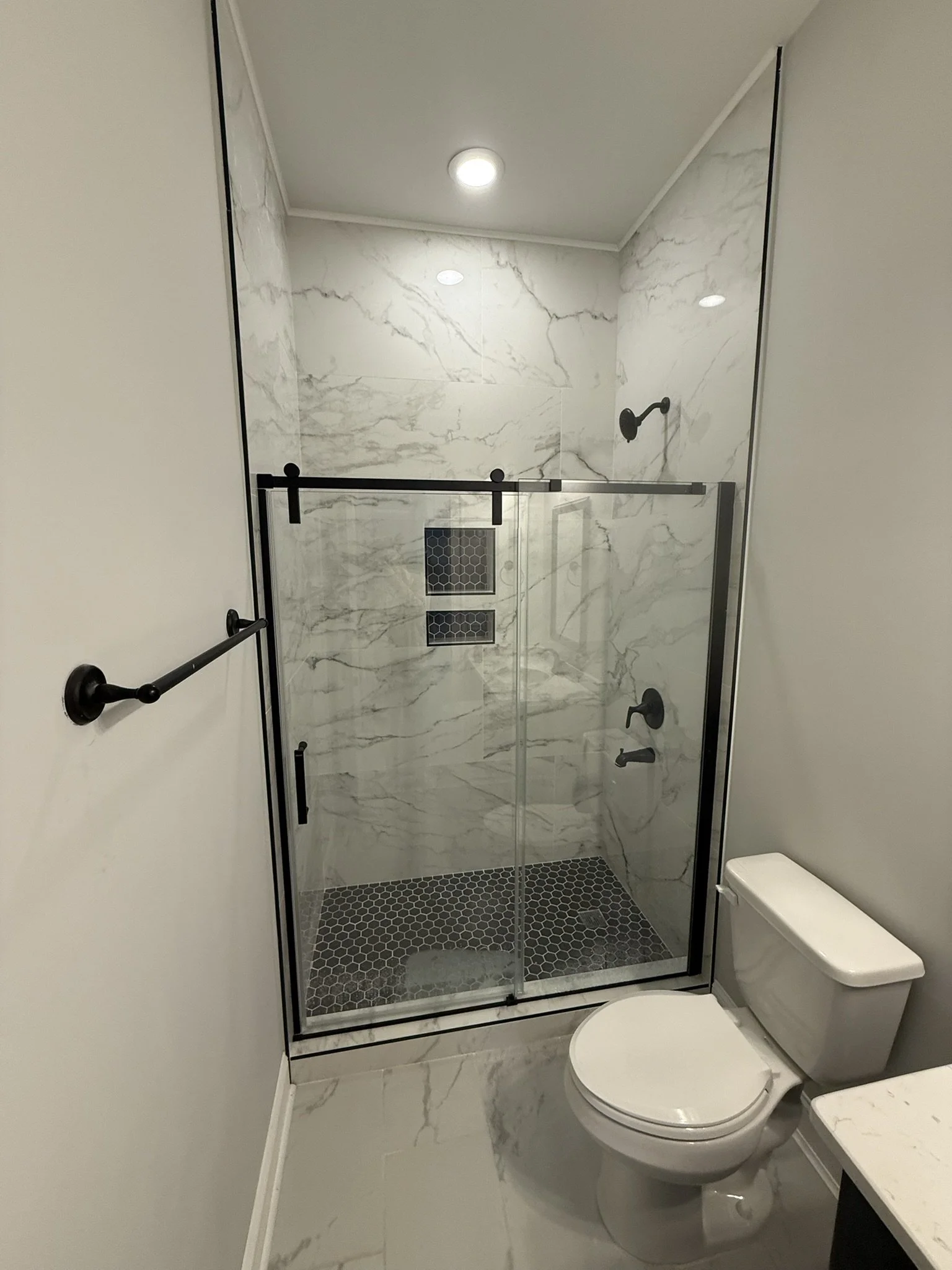 Bathroom with walk-in shower with black framed glass door, marble walls, and black fixtures, and a white toilet.