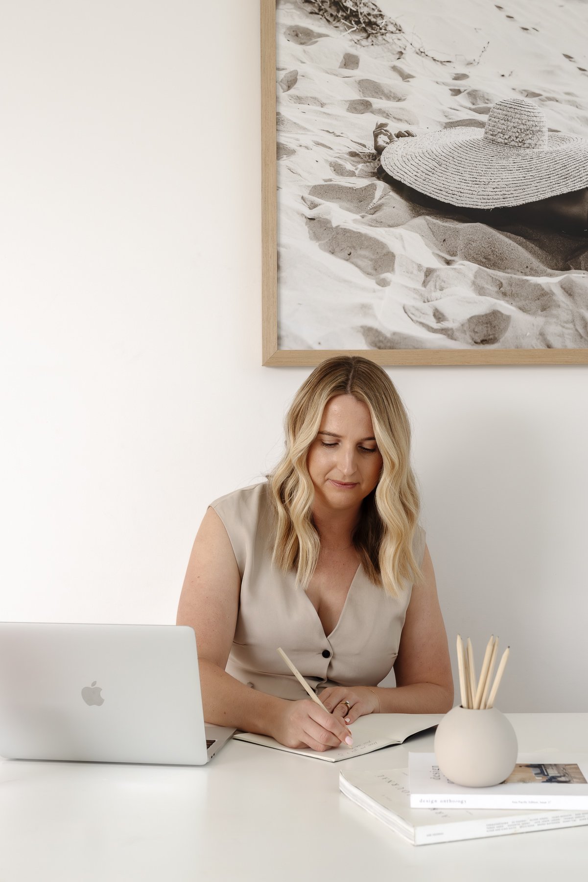 Hayley writing in a notebook at her desk with a laptop open