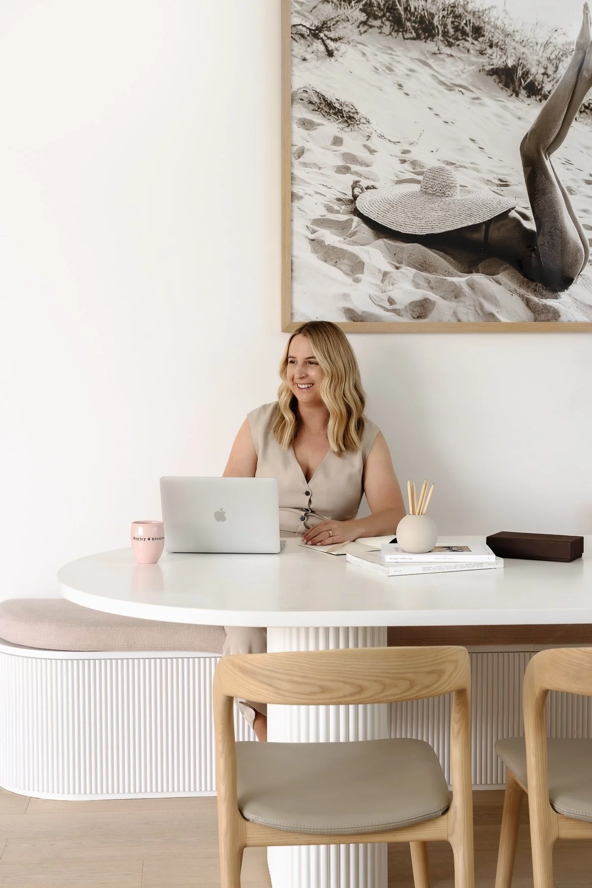 Hayley smiling at dining table with a laptop, pencil cup and branded mug