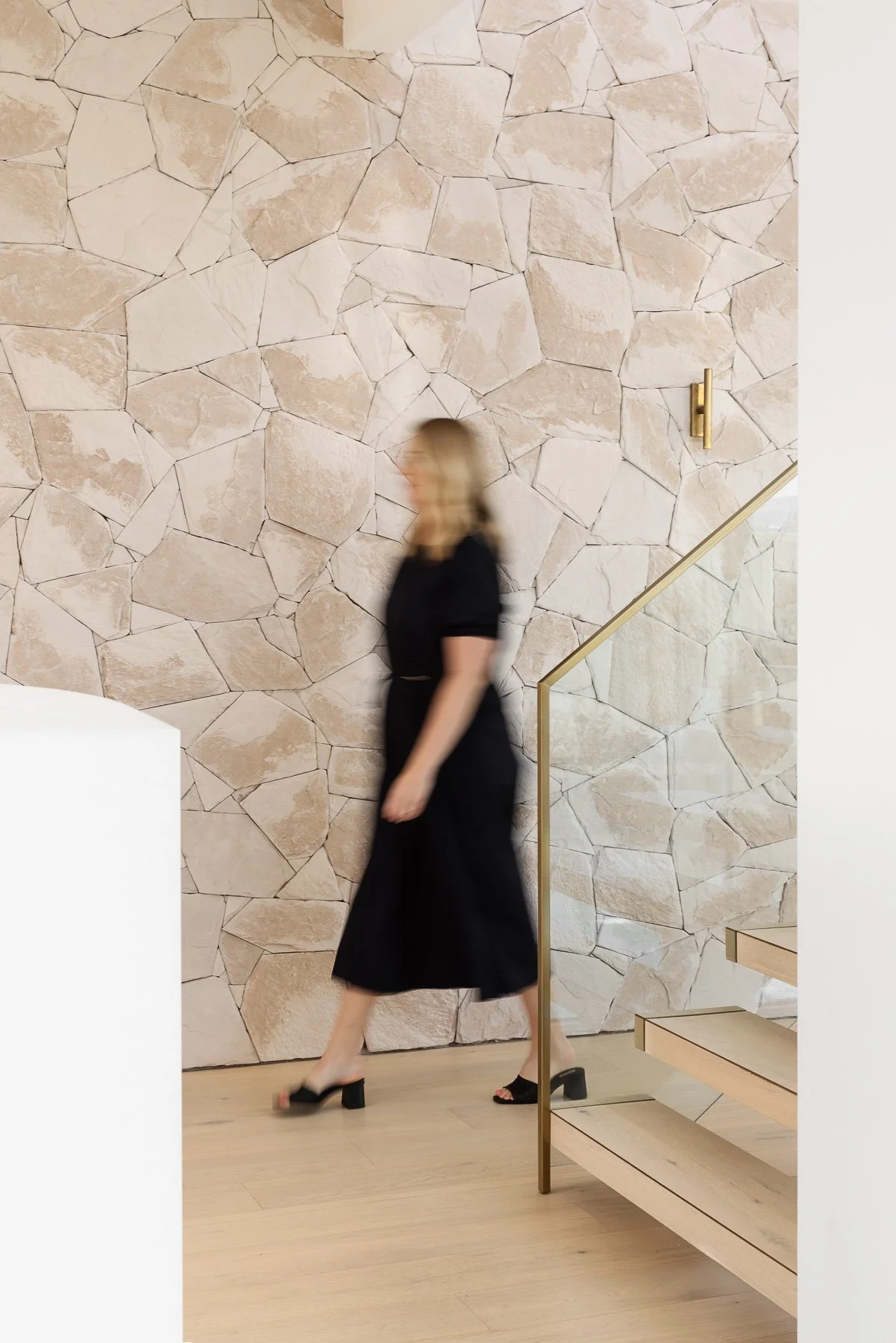 Hayley walking past a textured stone wall near a staircase