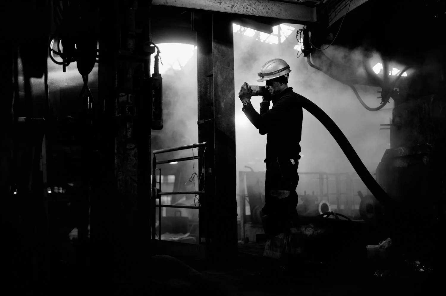 A firefighter wearing a helmet and protective gear working indoors with smoke and fog, holding a hose.