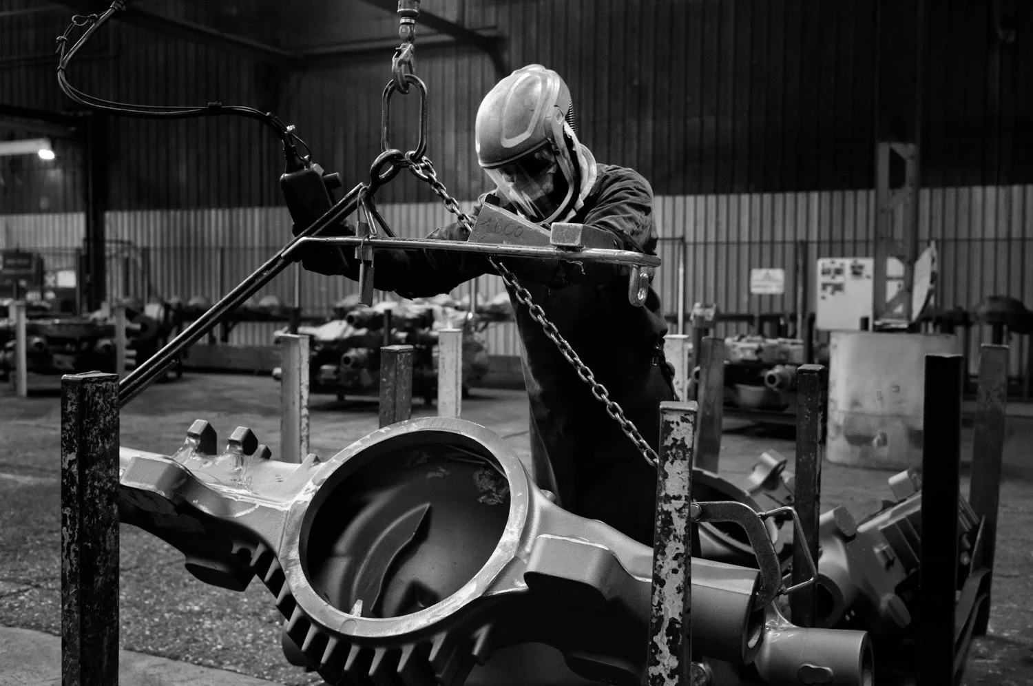 A worker wearing safety gear, including a helmet and face shield, is welding or examining a large metal engine component in a factory or workshop.