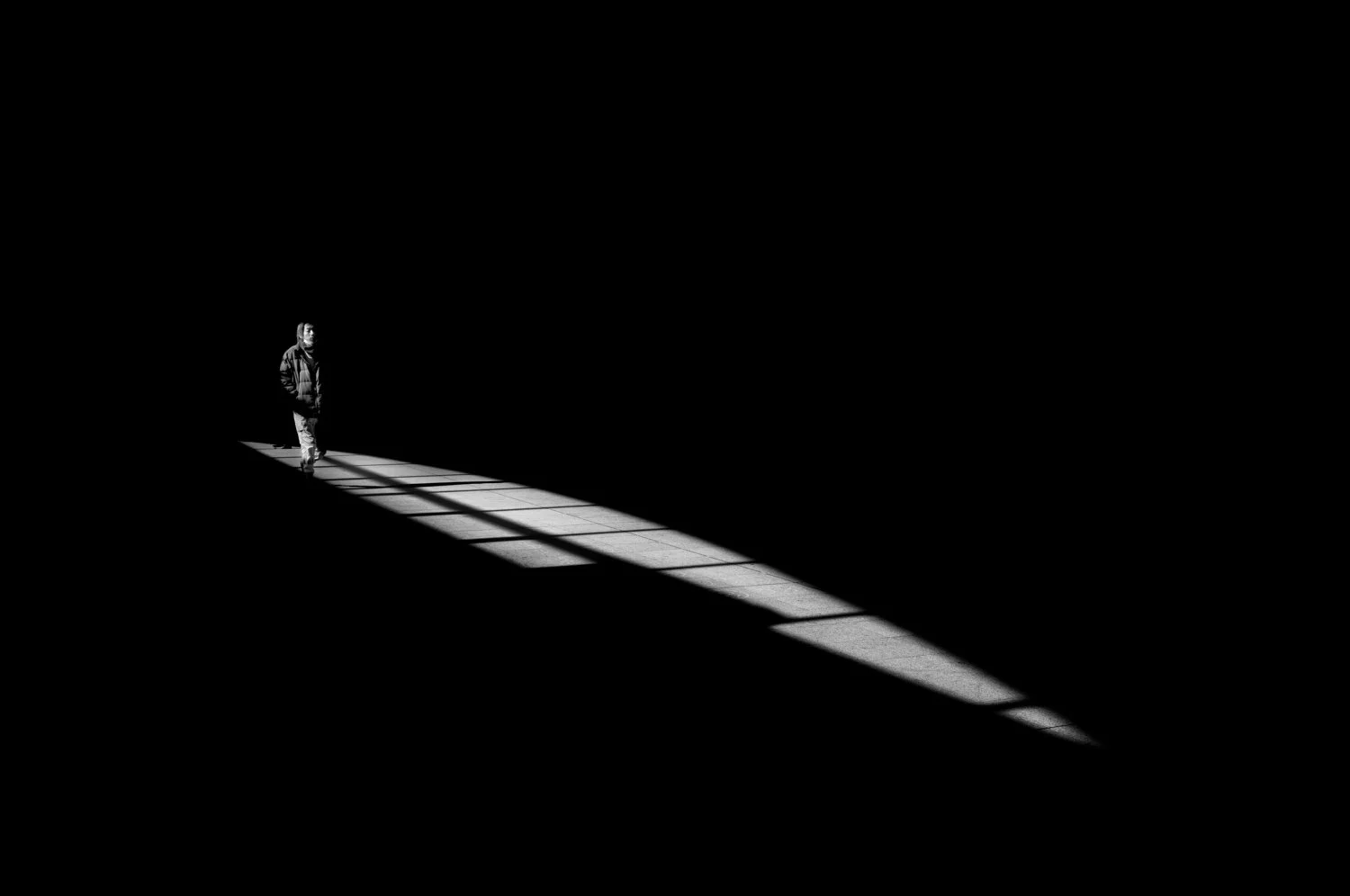 A person walking through a dark space with a chest-high window casting a strip of light on the floor.