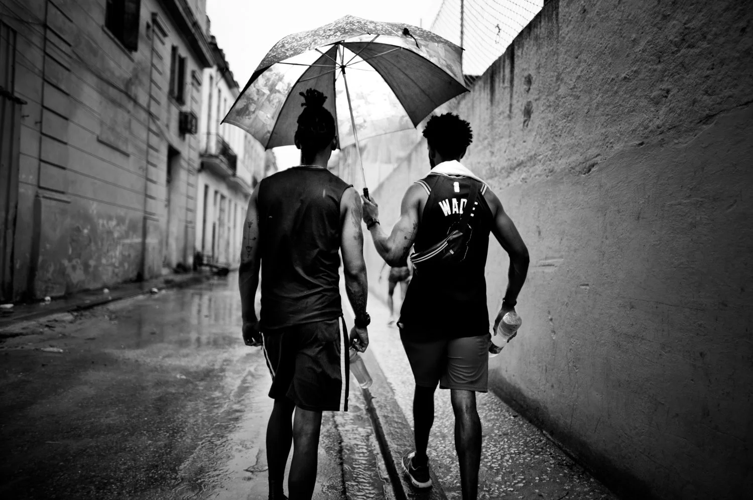 Two men walking in the rain, sharing an umbrella on a wet street.
