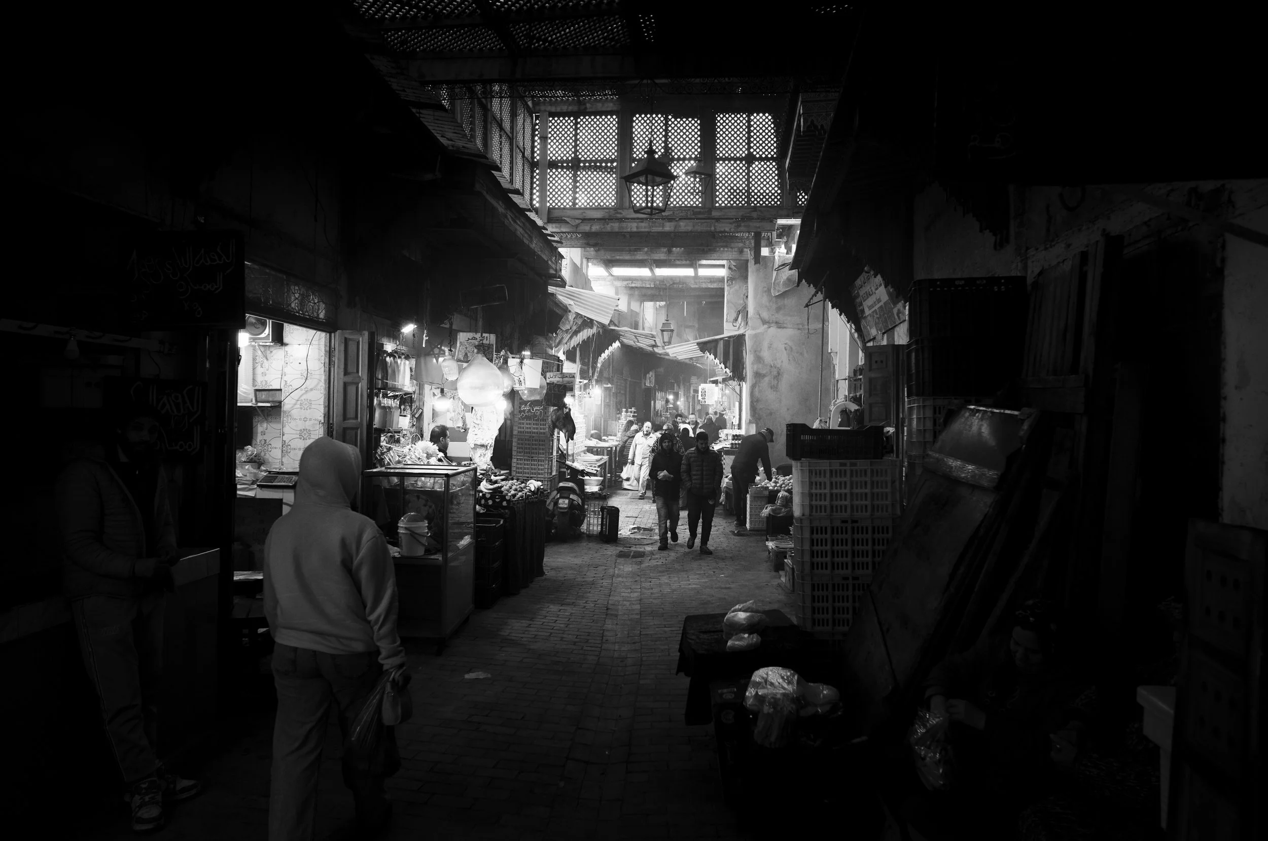 A bustling indoor market in black and white with vendors and shoppers browsing various goods.