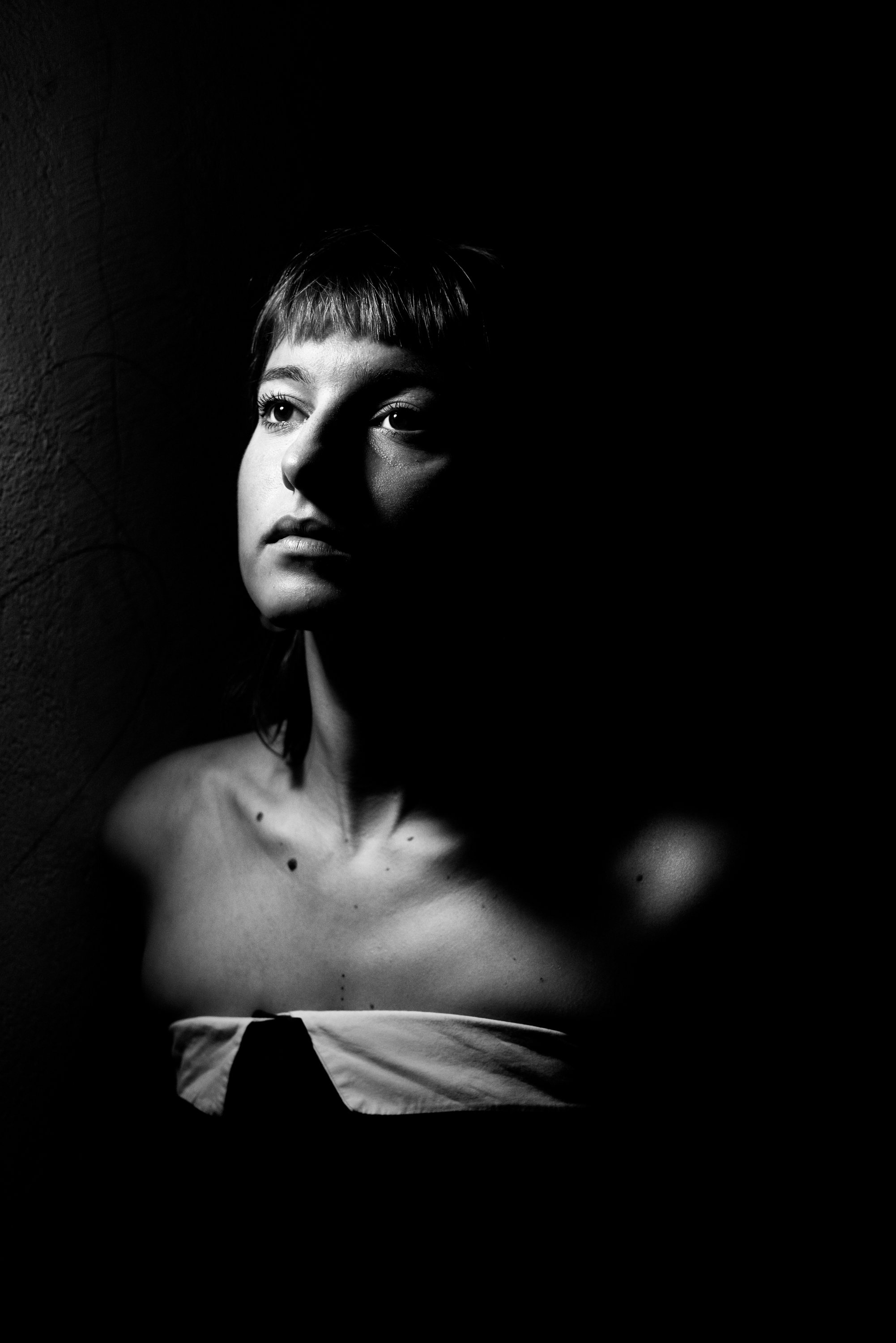 A portrait of a young woman with short hair, looking to the side, illuminated with dramatic lighting, in black and white.