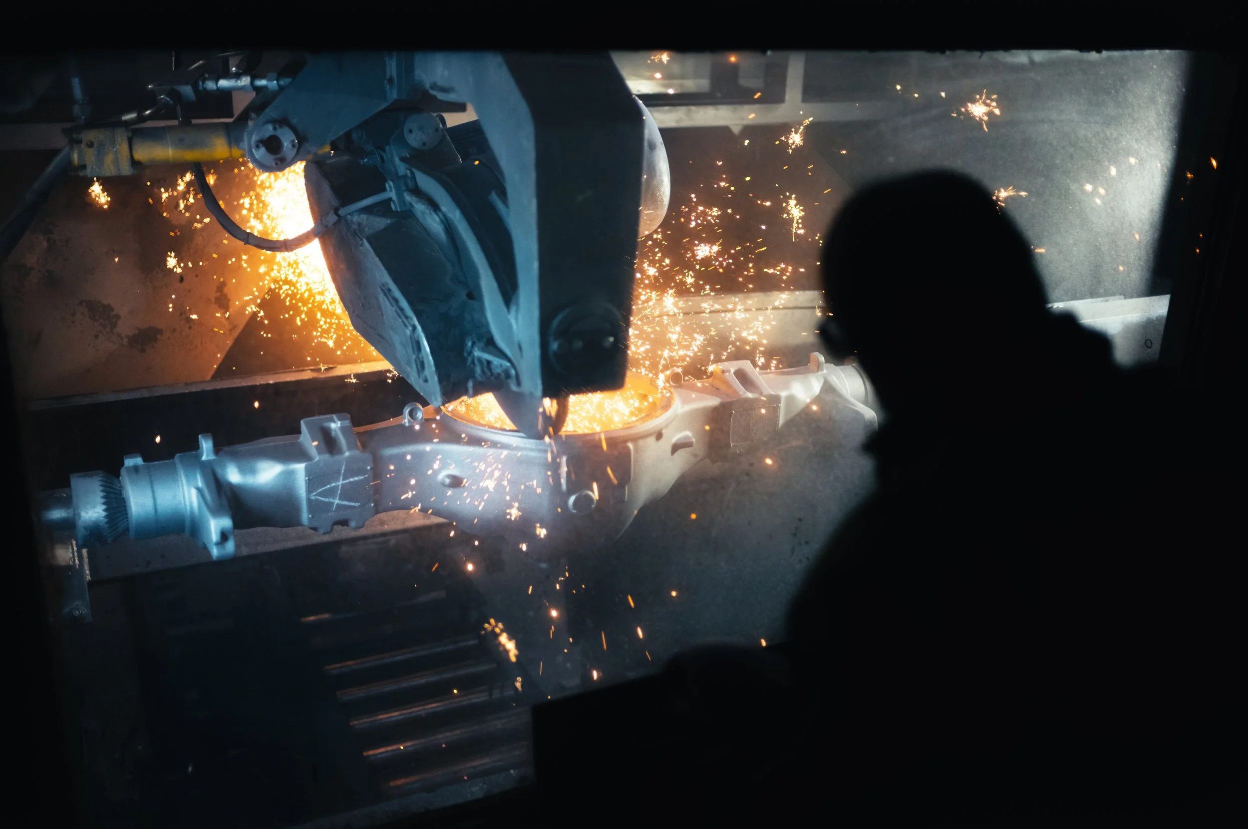 A robotic arm welds a metal component while sparks fly during the welding process.