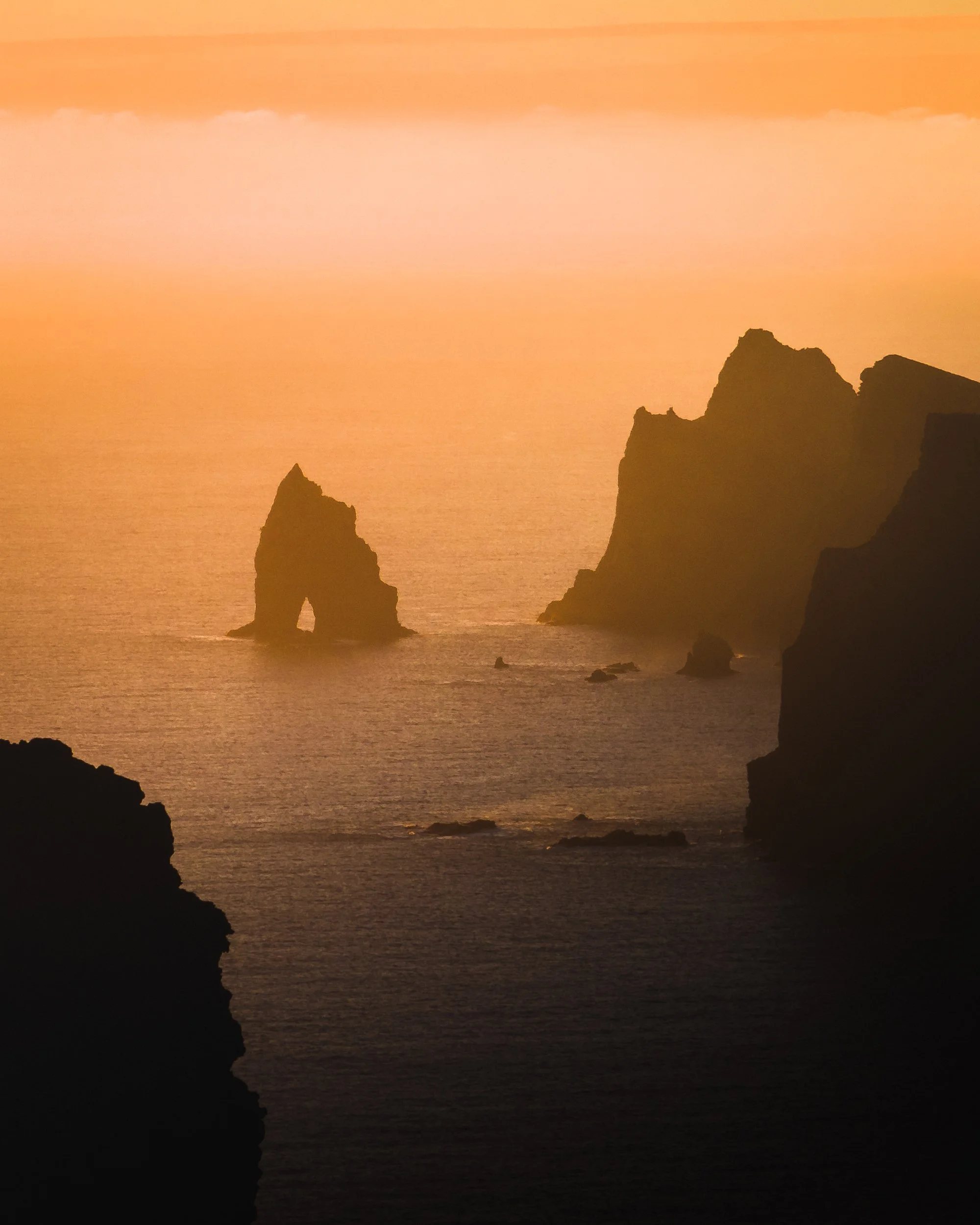 A scenic view of rocky sea stacks during sunset with orange and pink sky reflections on the water.