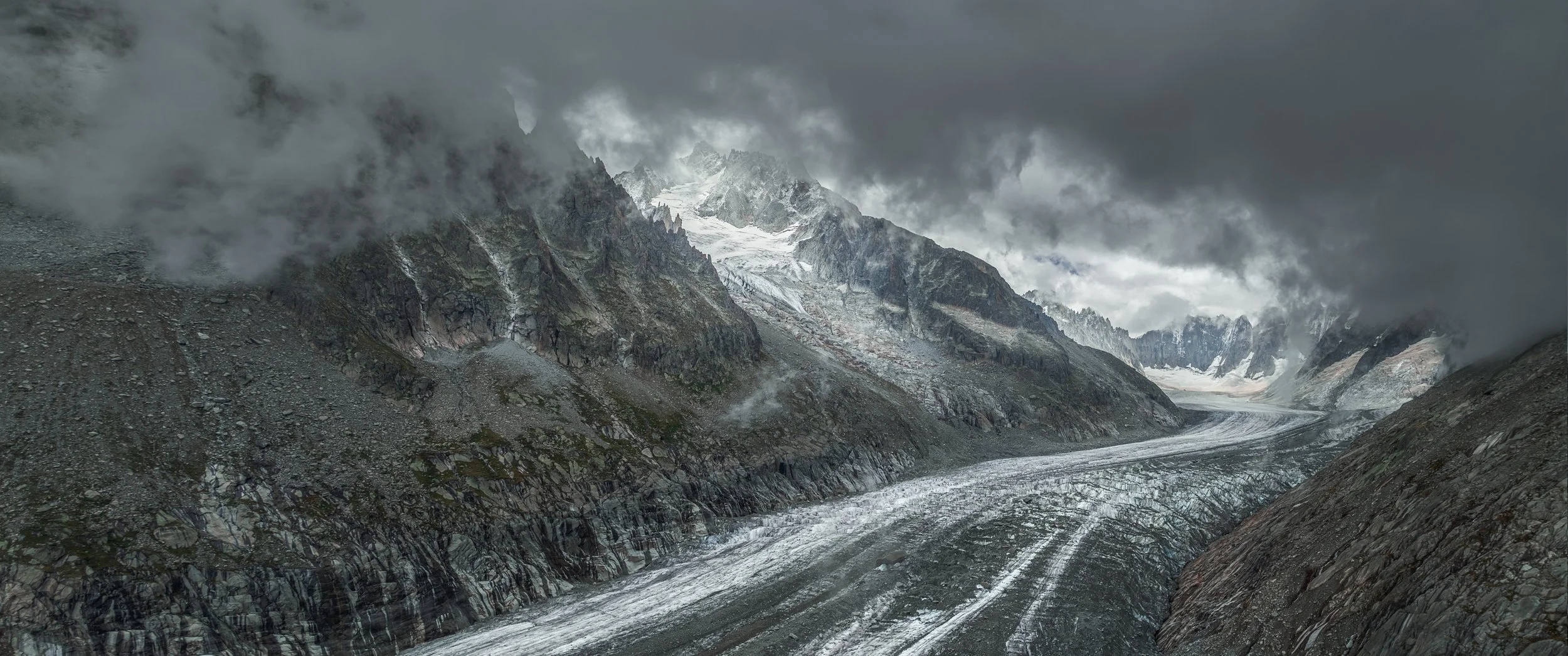 Overcast mountain landscape with glaciers and rocky slopes.