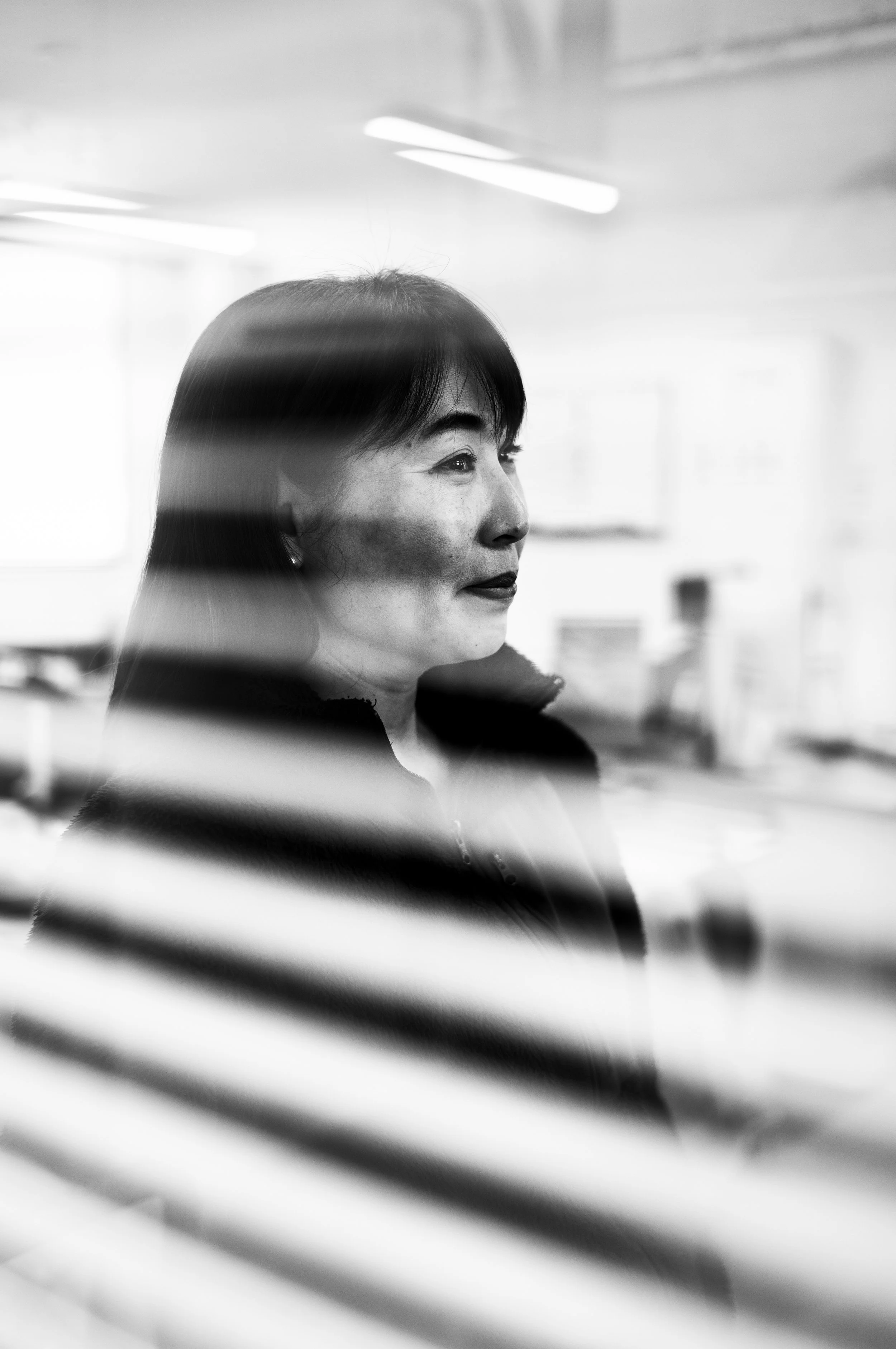 Black and white photo of a woman viewed through window blinds.