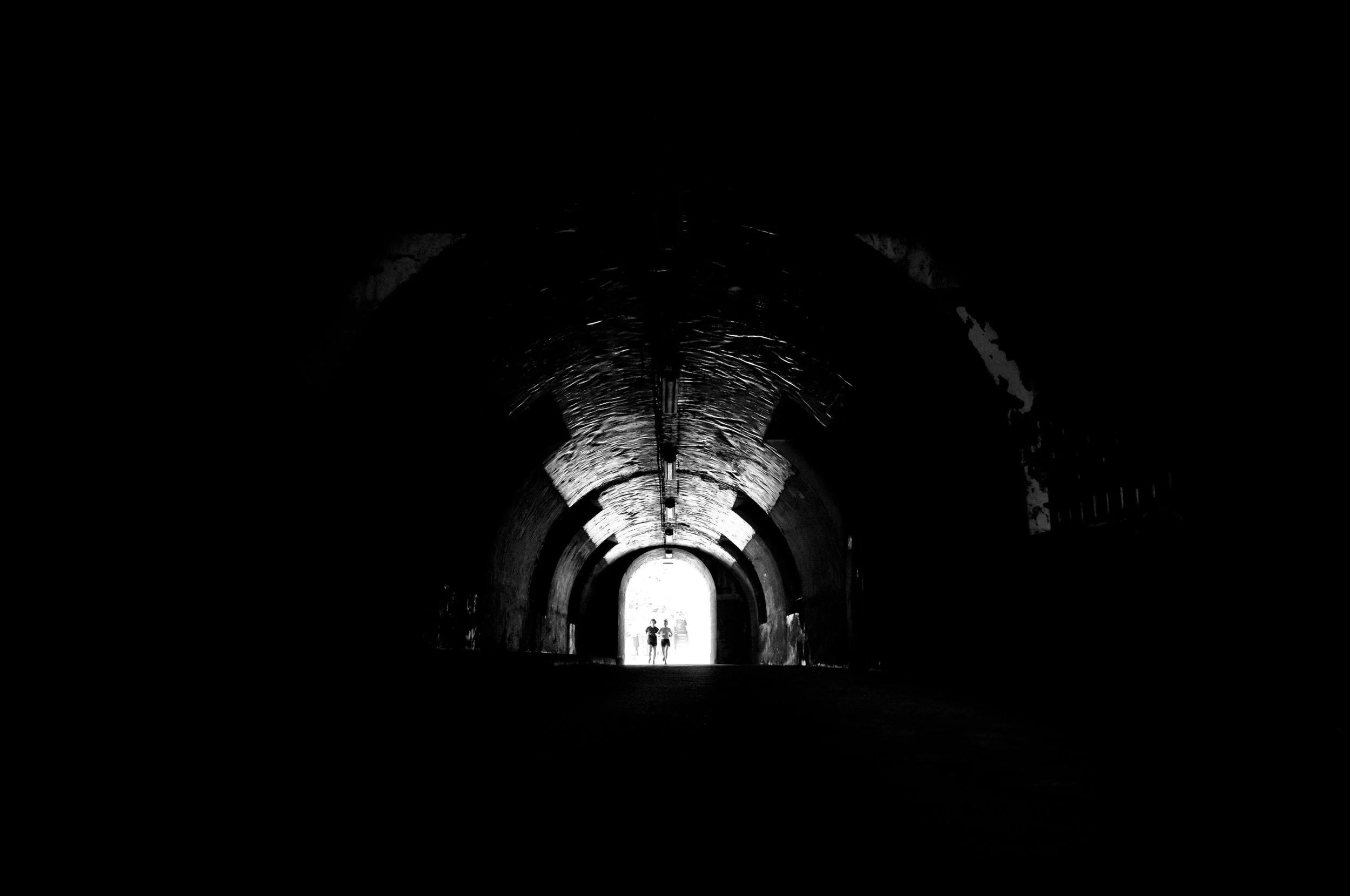 Two people walking through a dark tunnel towards bright daylight exit.