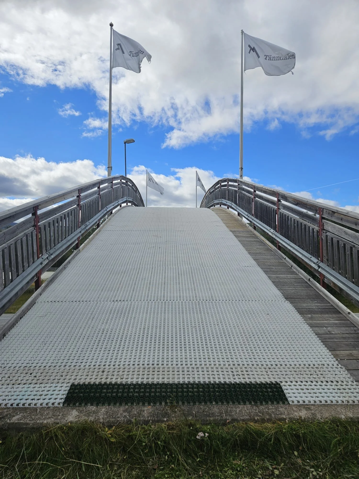 En uppåtriktad sned bild av en trappa med räcken, två vita flaggor med blå text, en på varje sida, mot en blå himmel med vita moln.