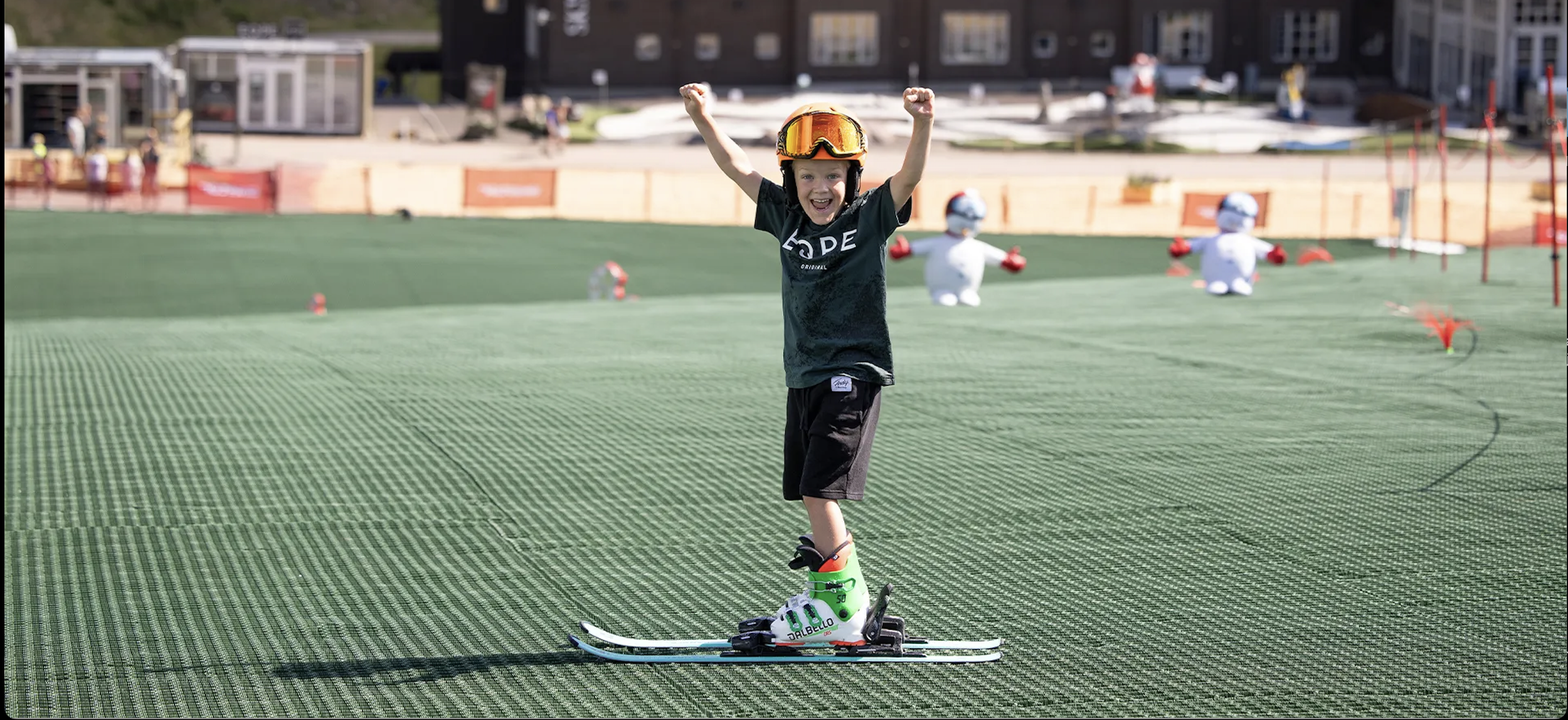 Ung pojke i skidutrustning som firar med armarna i luften på en snötäckt sluttning