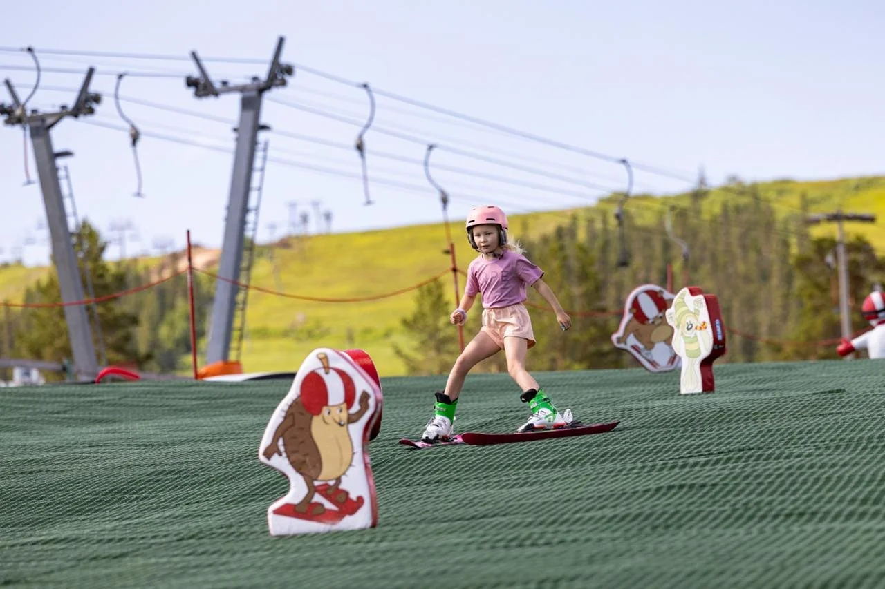 Ung pojke i skidutrustning som firar med armarna i luften på en snötäckt sluttning