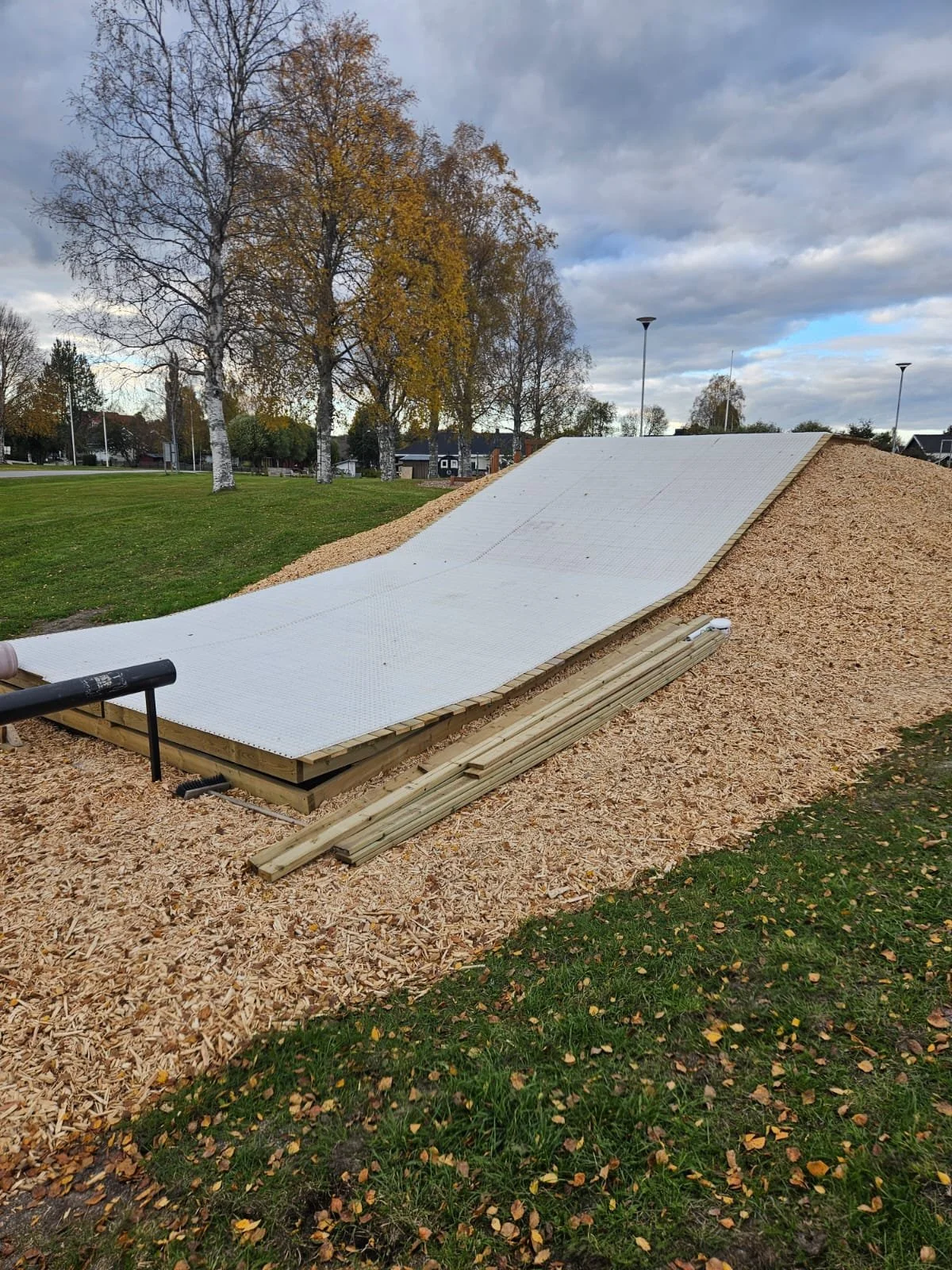 Uppbyggd konstgjord åkattrappa i ett parkeringsområde med träd och himmel i bakgrunden.