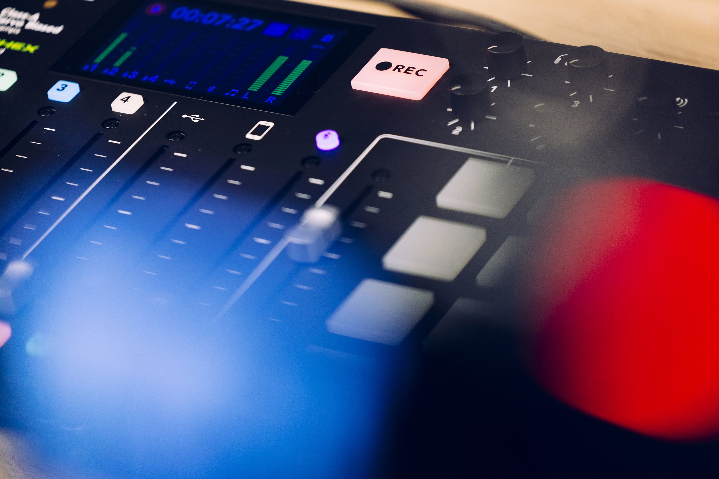 Close-up of a podcast digital mixer with sliders, knobs, and a colorful display.