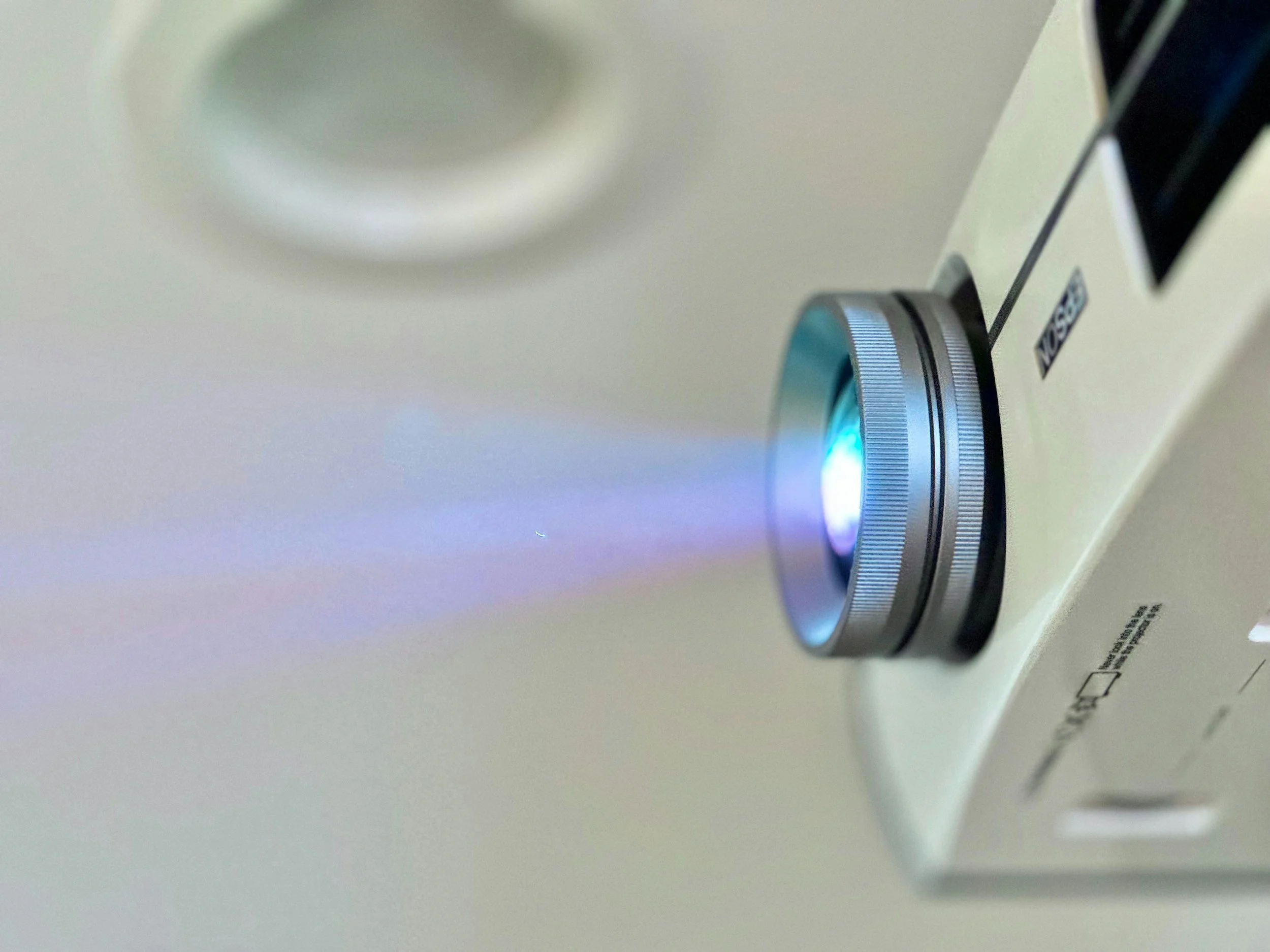 Close-up of a white camera projecting a light blue beam onto a white surface.