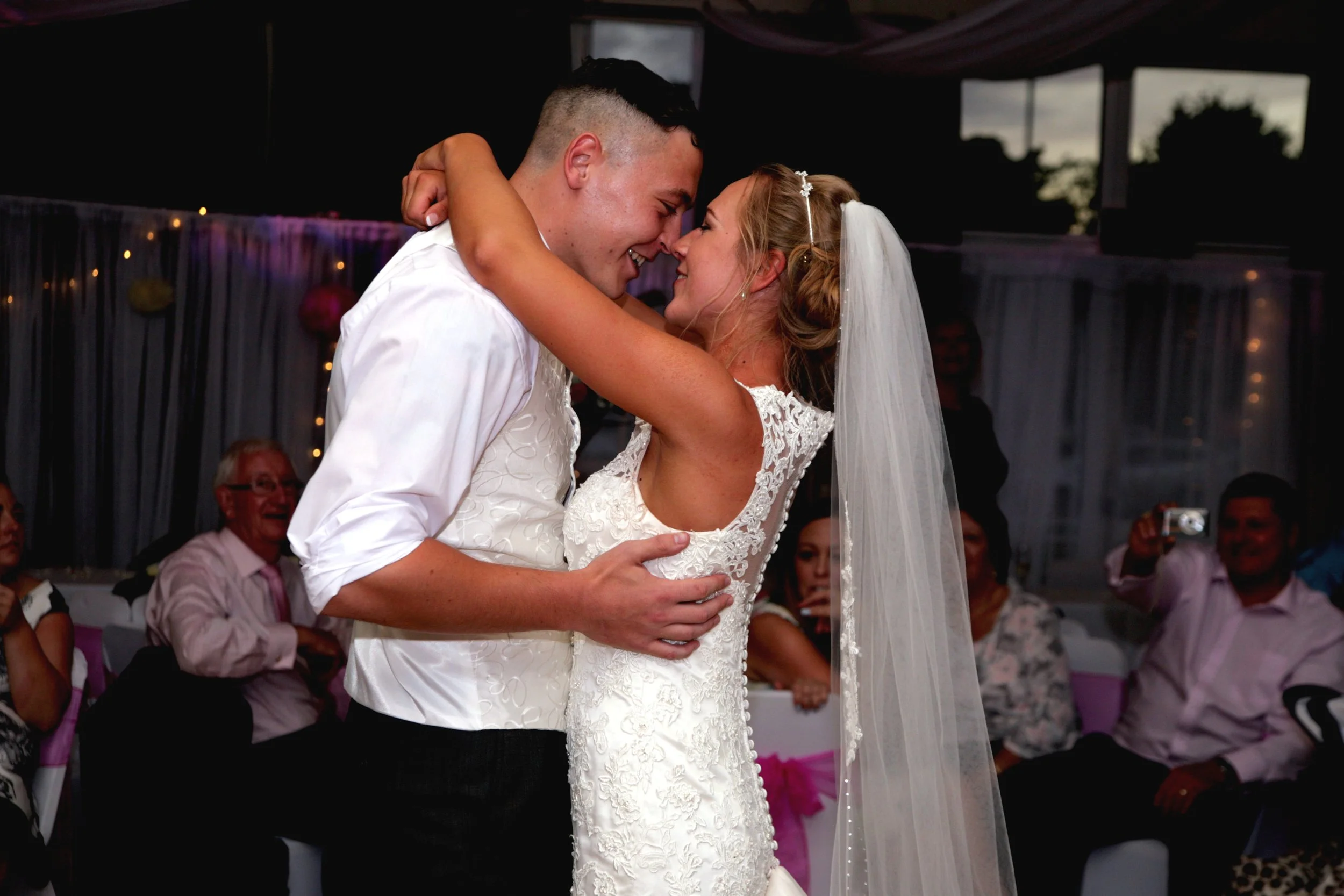 A bride and groom sharing a dance at their wedding reception, surrounded by guests watching and smiling.