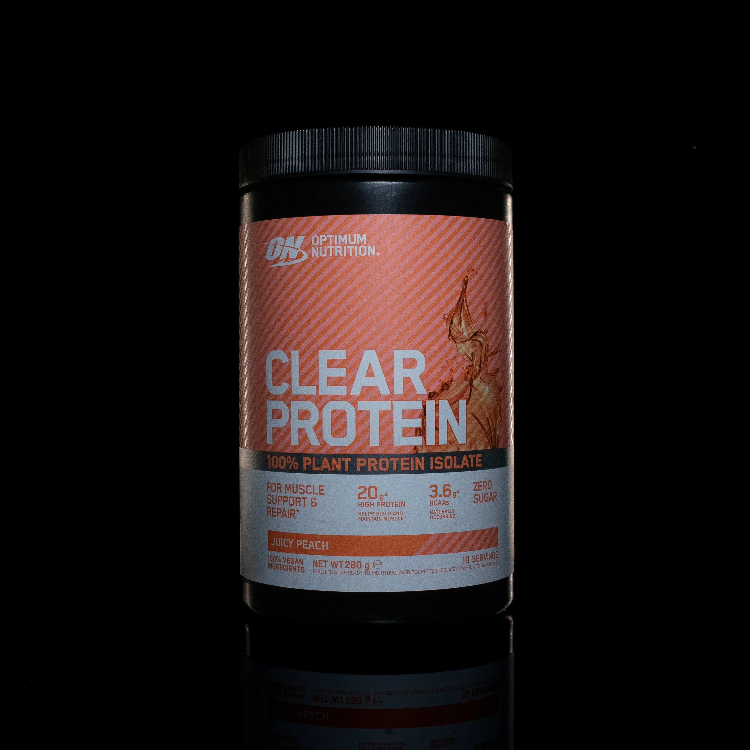A container of Optimum Nutrition Clear Protein with a black lid and pink label, set against a black background with a reflection of the container visible below.
