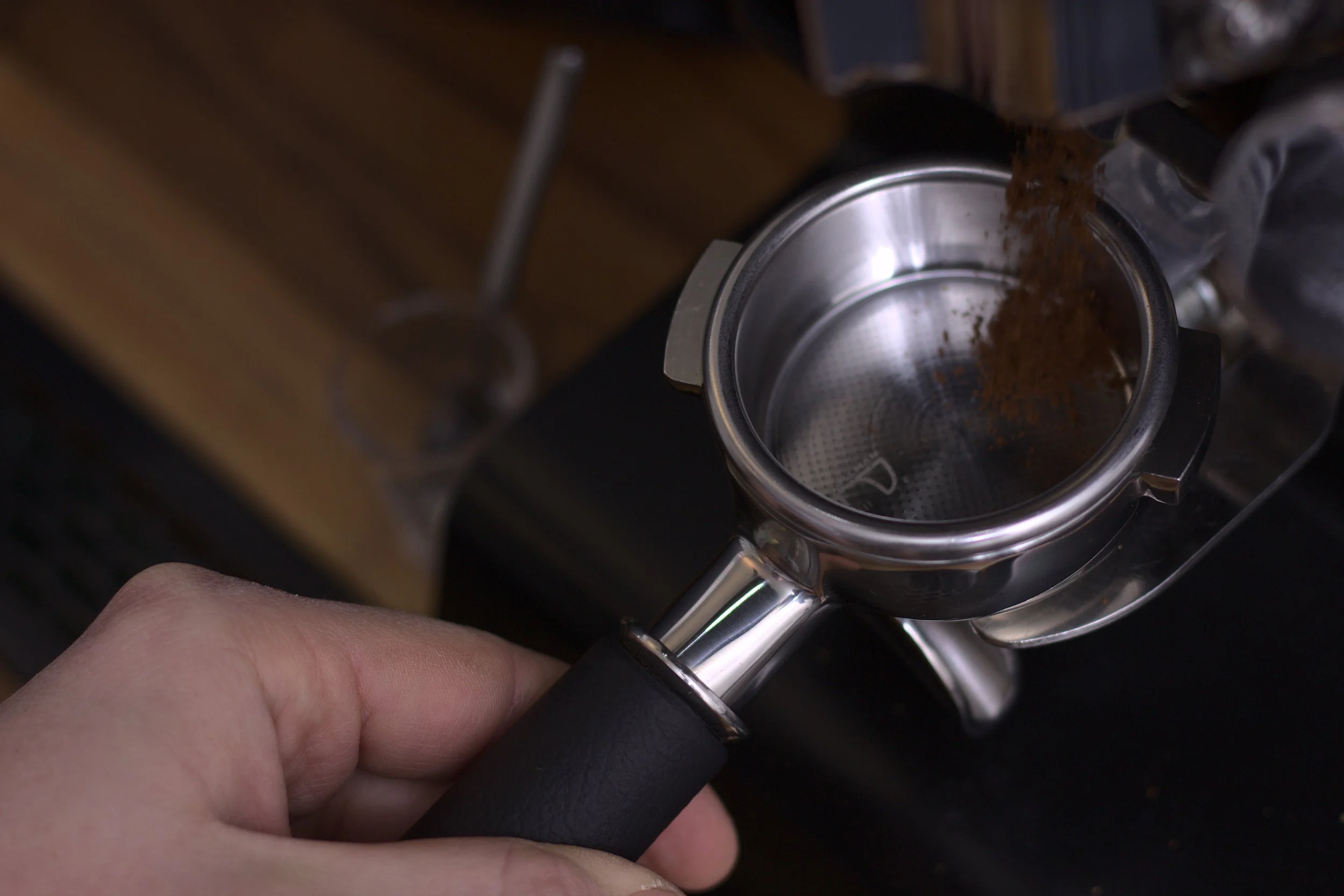 A person holding a portafilter as it is filled with ground coffee from a coffee grinder.
