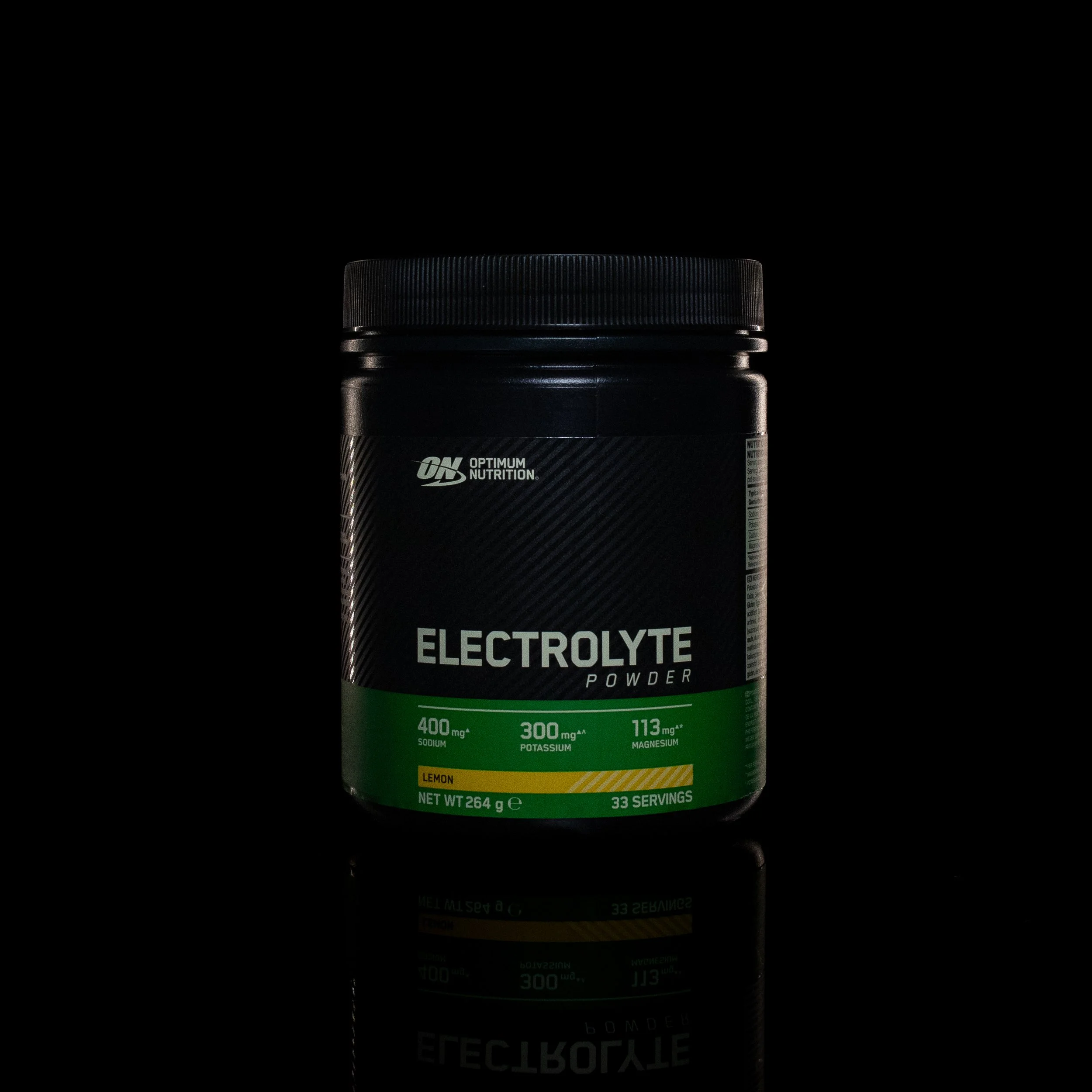 A container of Optimum Nutrition Electrolyte Powder with a black lid, labeled with green and yellow accents, set against a black background with a reflection of the container visible below.