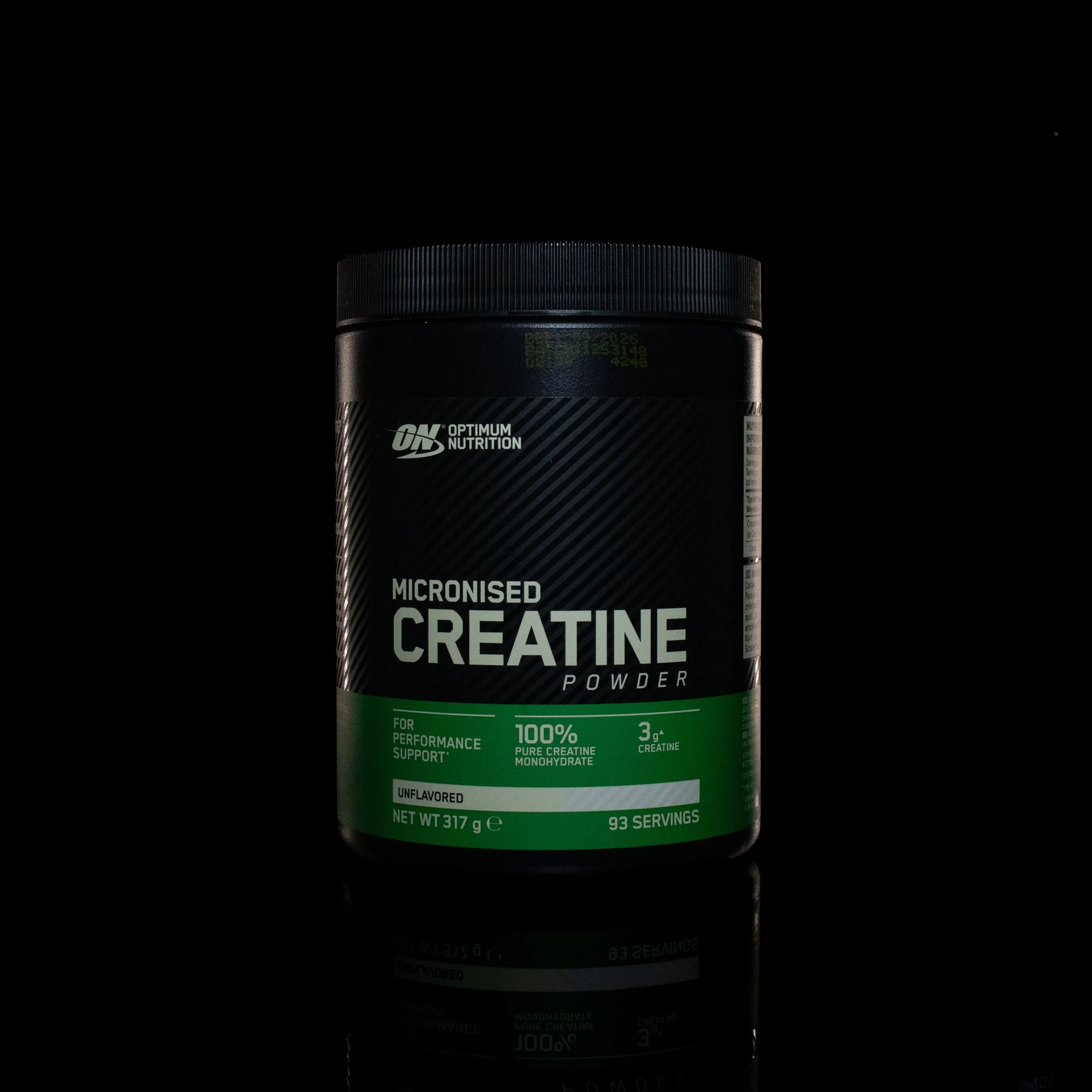 A container of Optimum Nutrition Micronized Creatine Powder with a green label, set against a black background with a reflection of the container visible below.