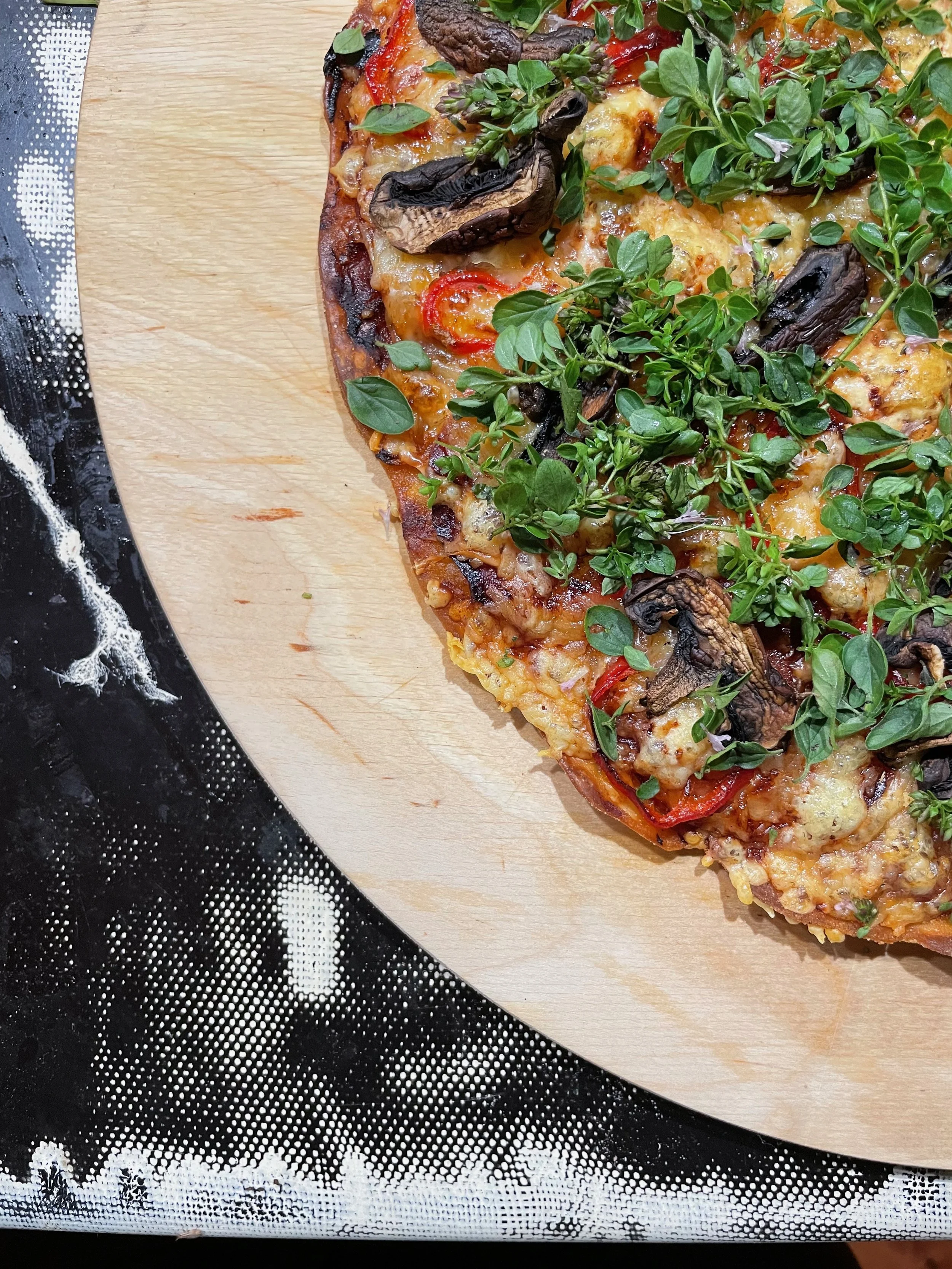 Une part de pizza aux champignons, tomates et herbes sur une planche en bois.