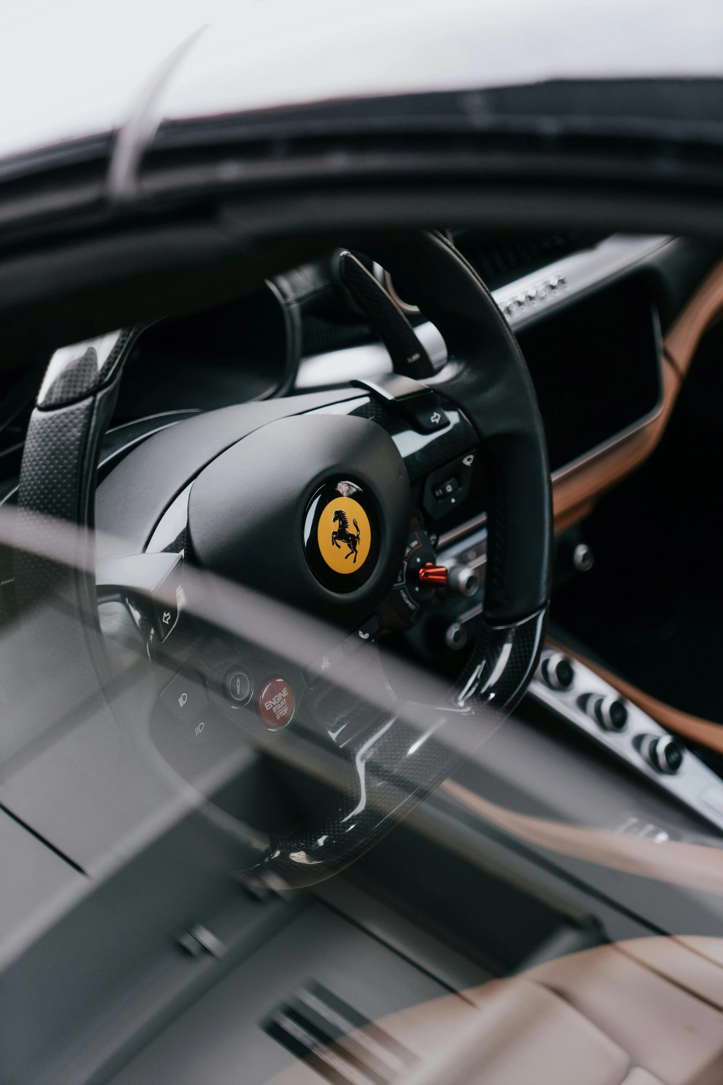 Close-up of a Ferrari car interior focusing on the steering wheel with Ferrari logo, dashboard, and driving controls.