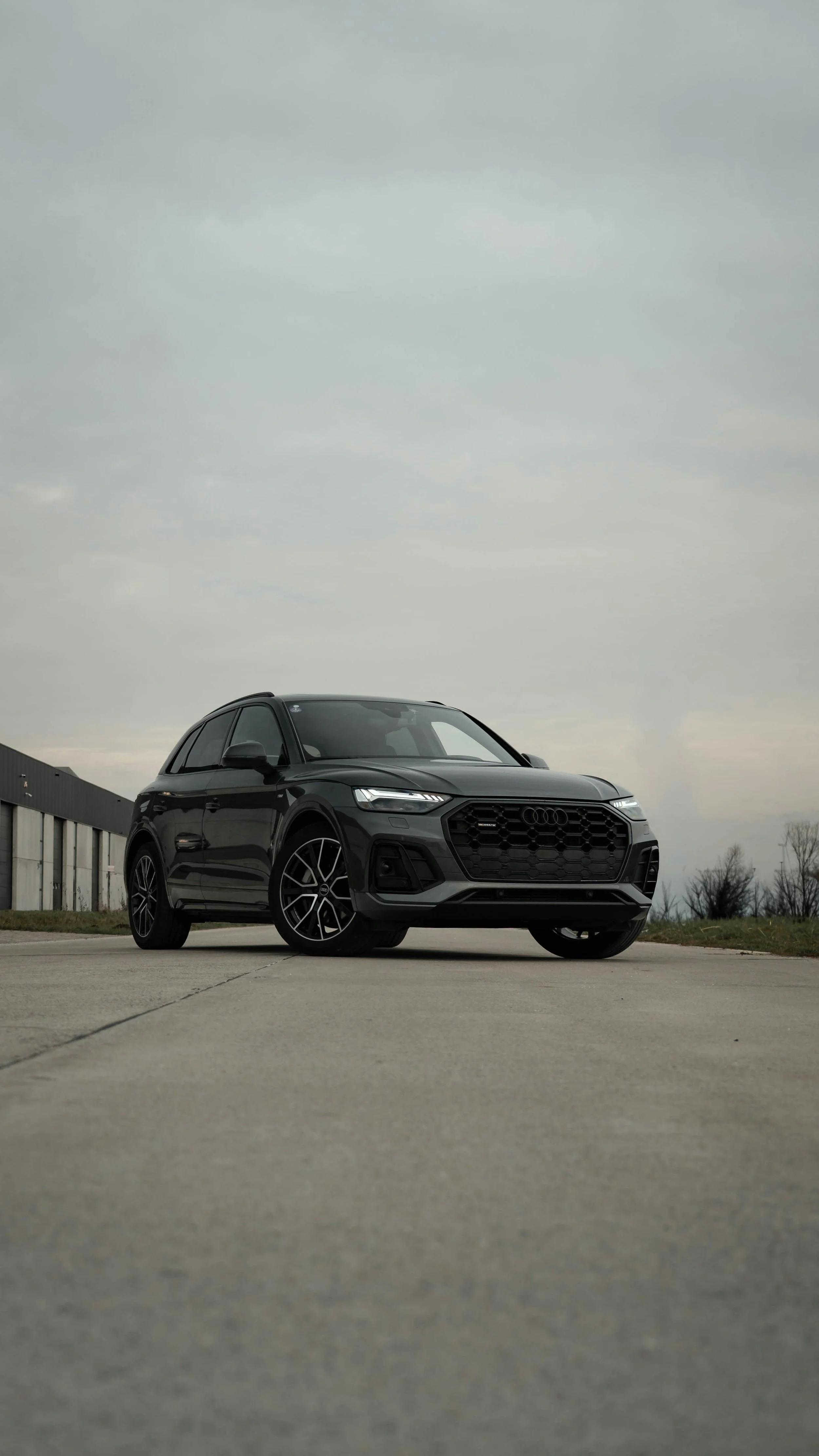 A black Audi SUV parked on a concrete surface outdoors under a cloudy sky.