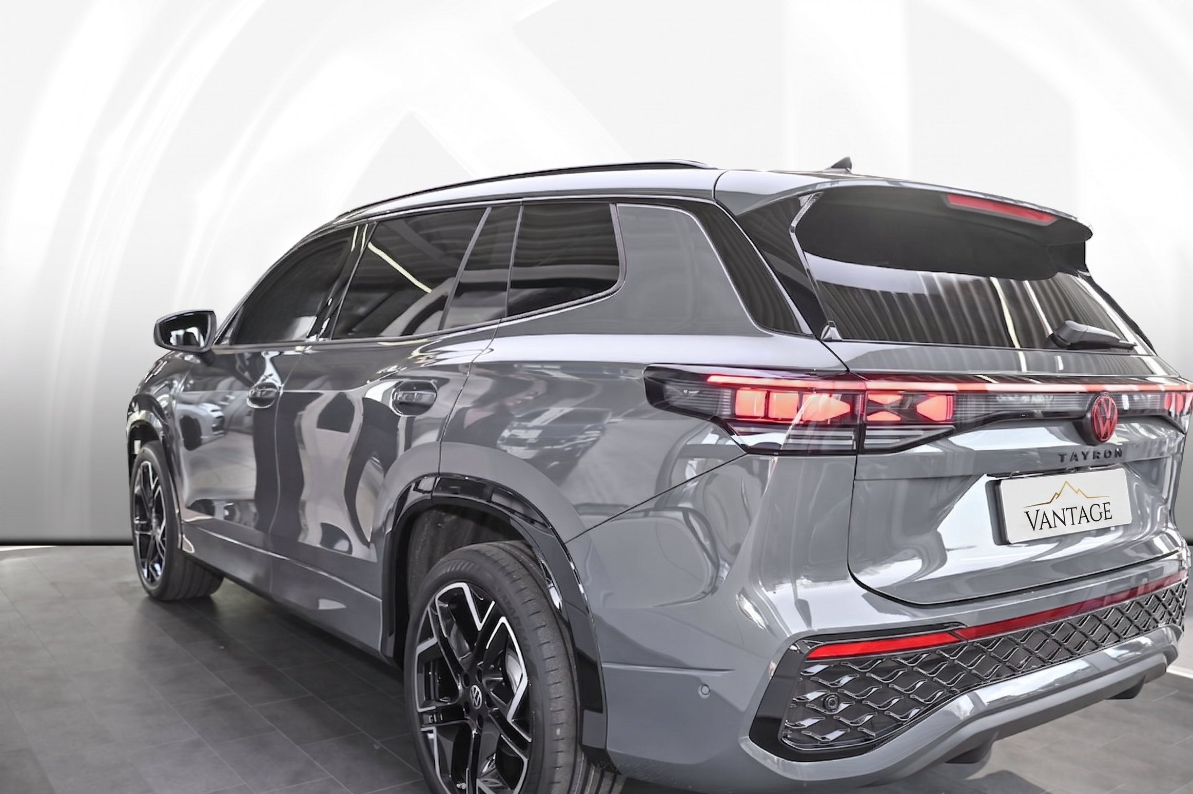 A silver Volkswagen Tayron SUV showcased indoors with a VANTAGE license plate, reflecting a modern design with sleek lines, black windows, and stylish wheels.