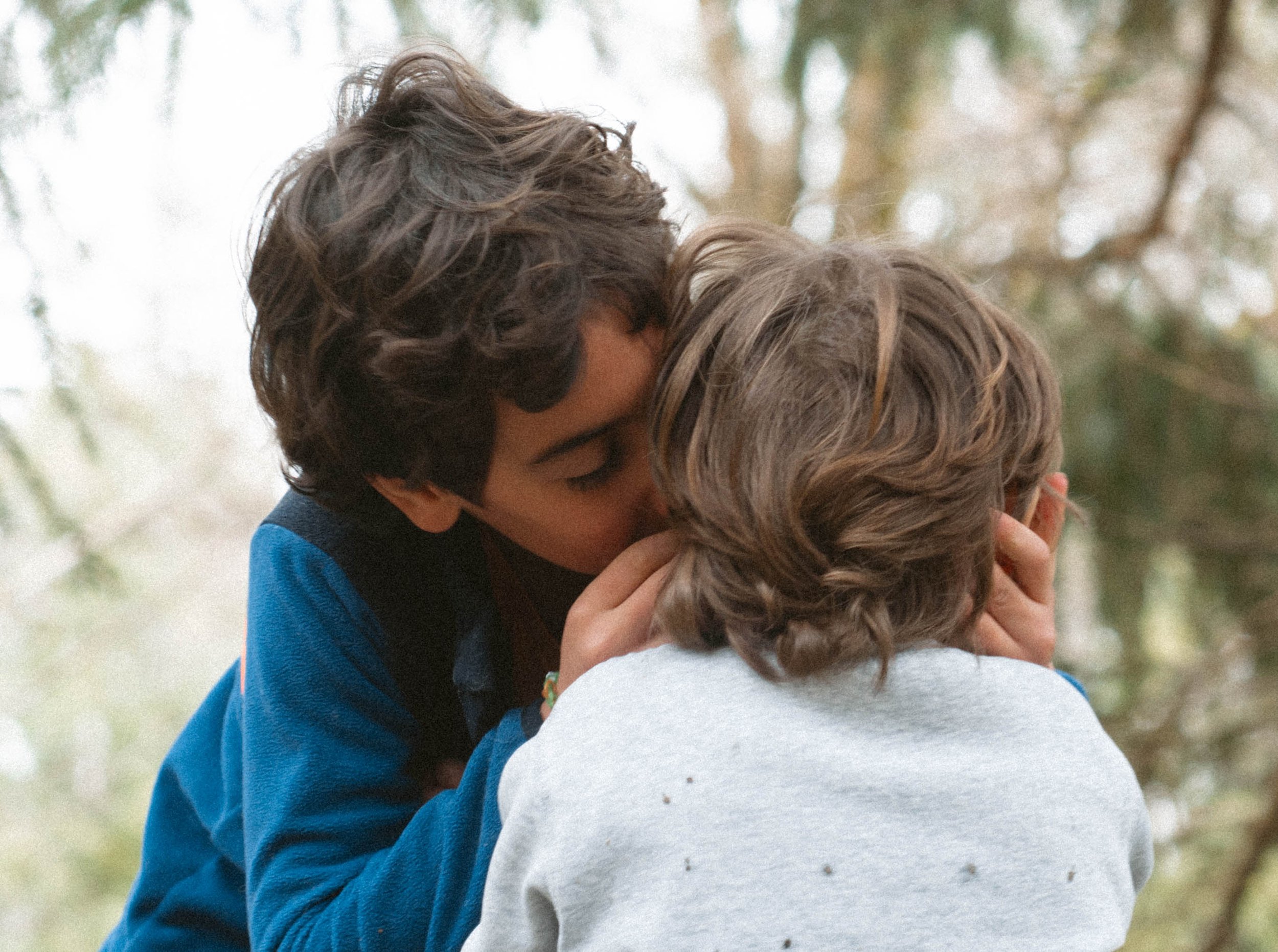 Un jeune garçon racontant un secret à un autre, sous un arbre, par une journée ensoleillée.