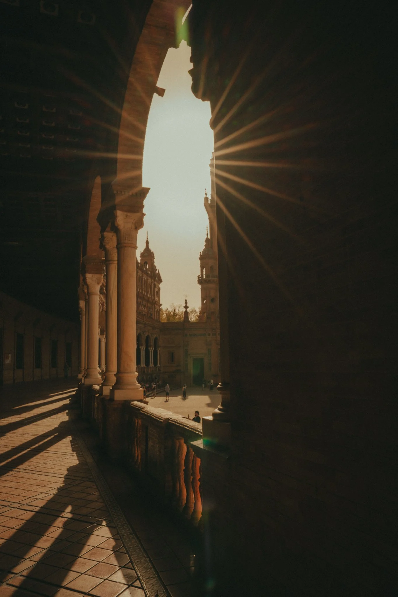 Sunlight streams through arches in a historic courtyard, casting long shadows and creating a starburst effect.