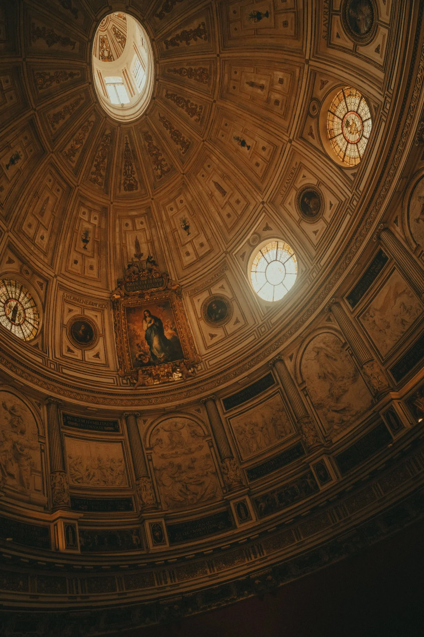 Interior view of a domed ceiling with ornate decorations, windows, and a portrait.