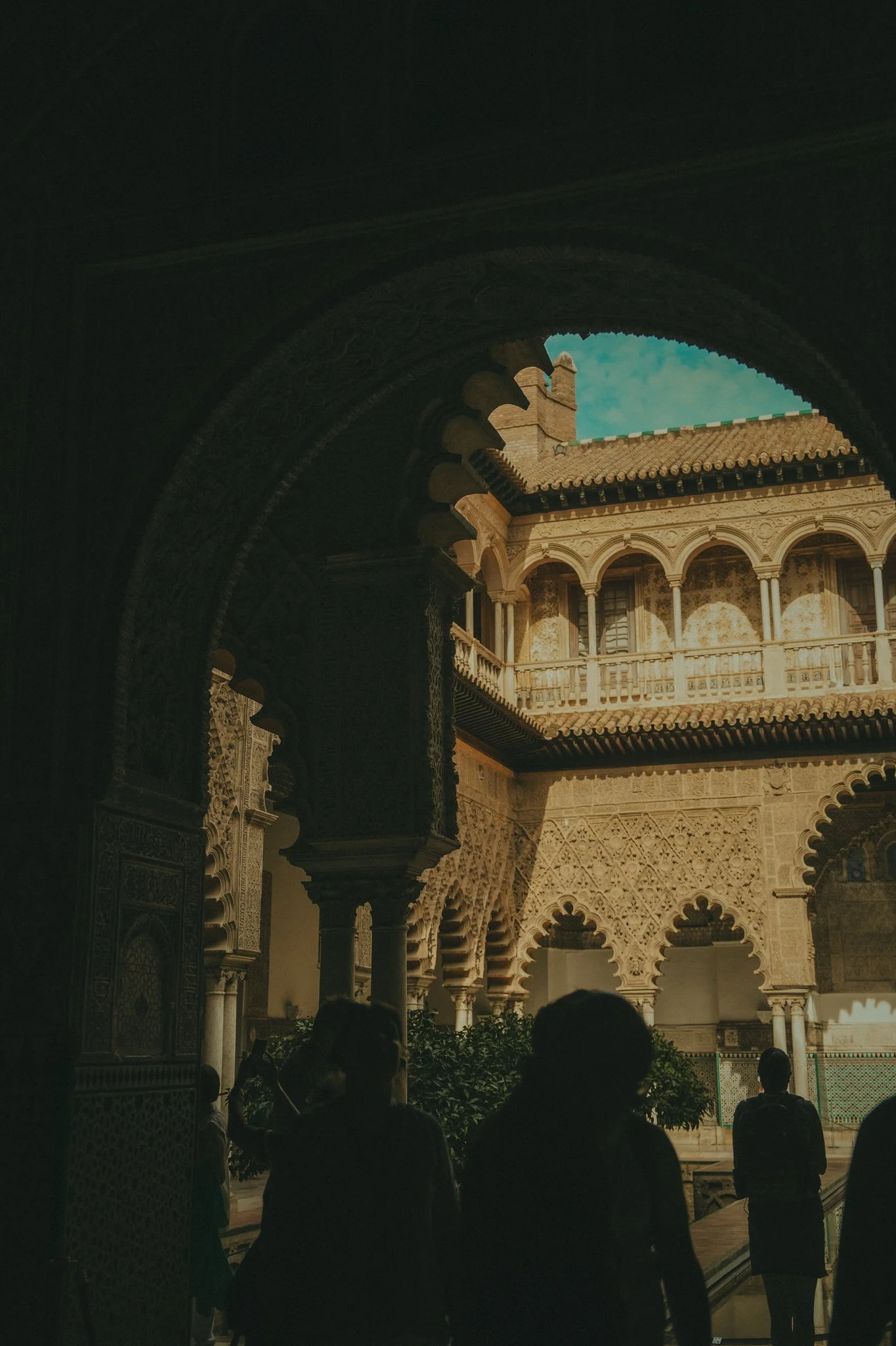 The photo shows an interior courtyard of a historical building with intricate architectural details, arches, and columns, with some people standing and observing the space.