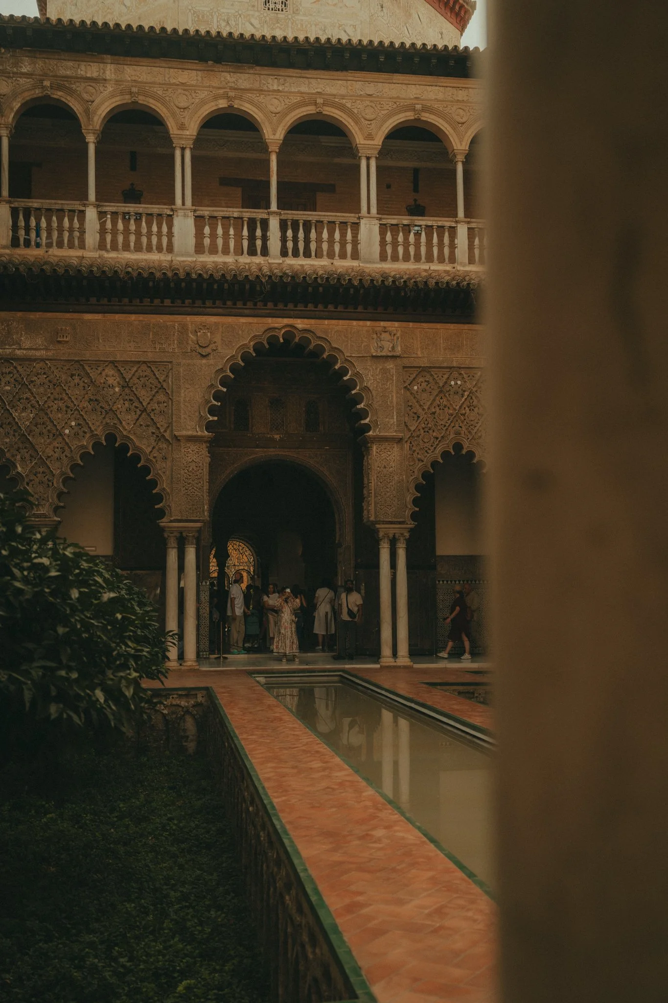 People gathered in an ornate courtyard with intricate architectural details, arches, and a water feature, under warm lighting.