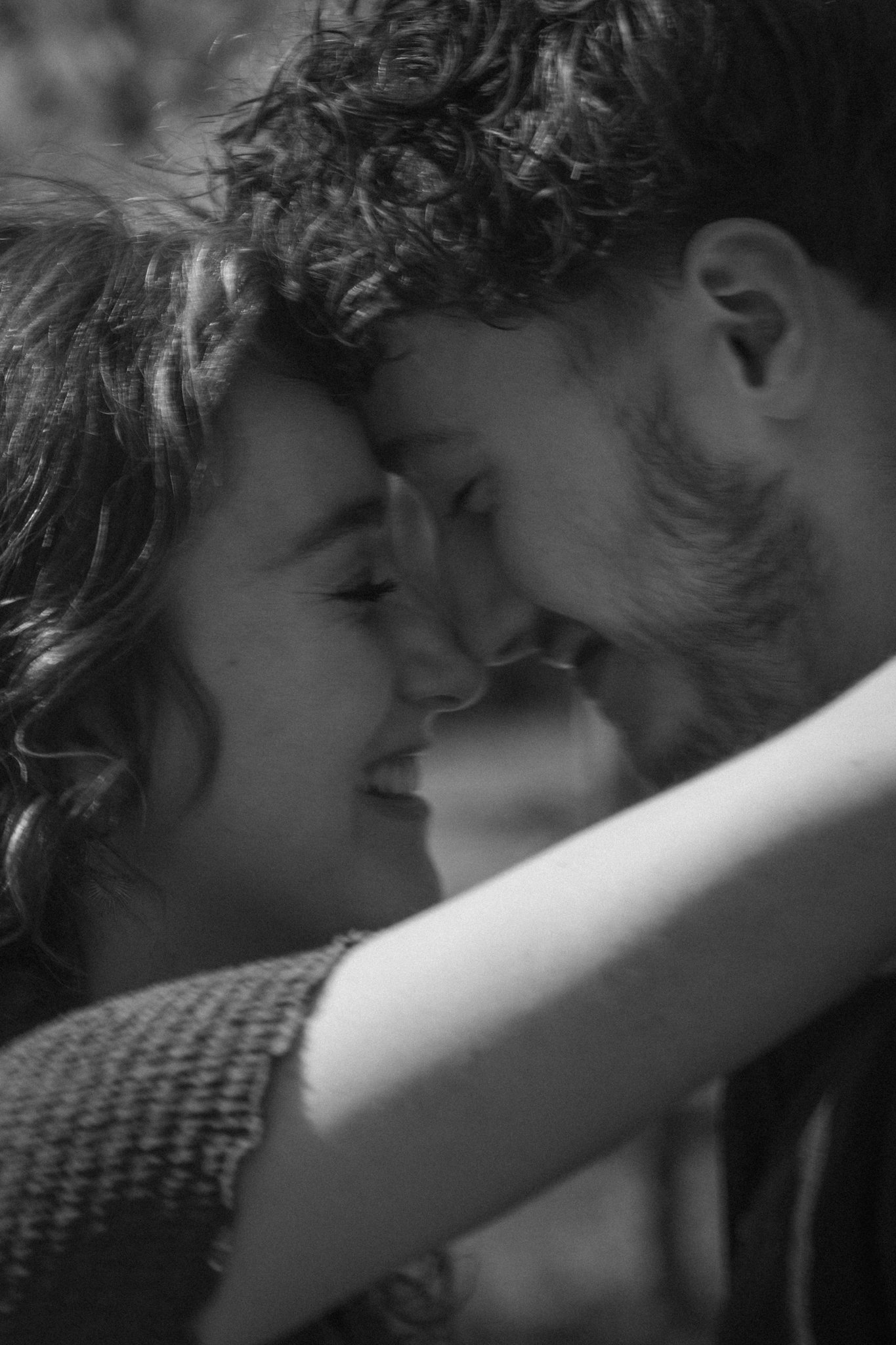 Close-up black and white photograph of two children with their foreheads touching, showing delicate expressions and curly hair, creating an intimate and tender scene.