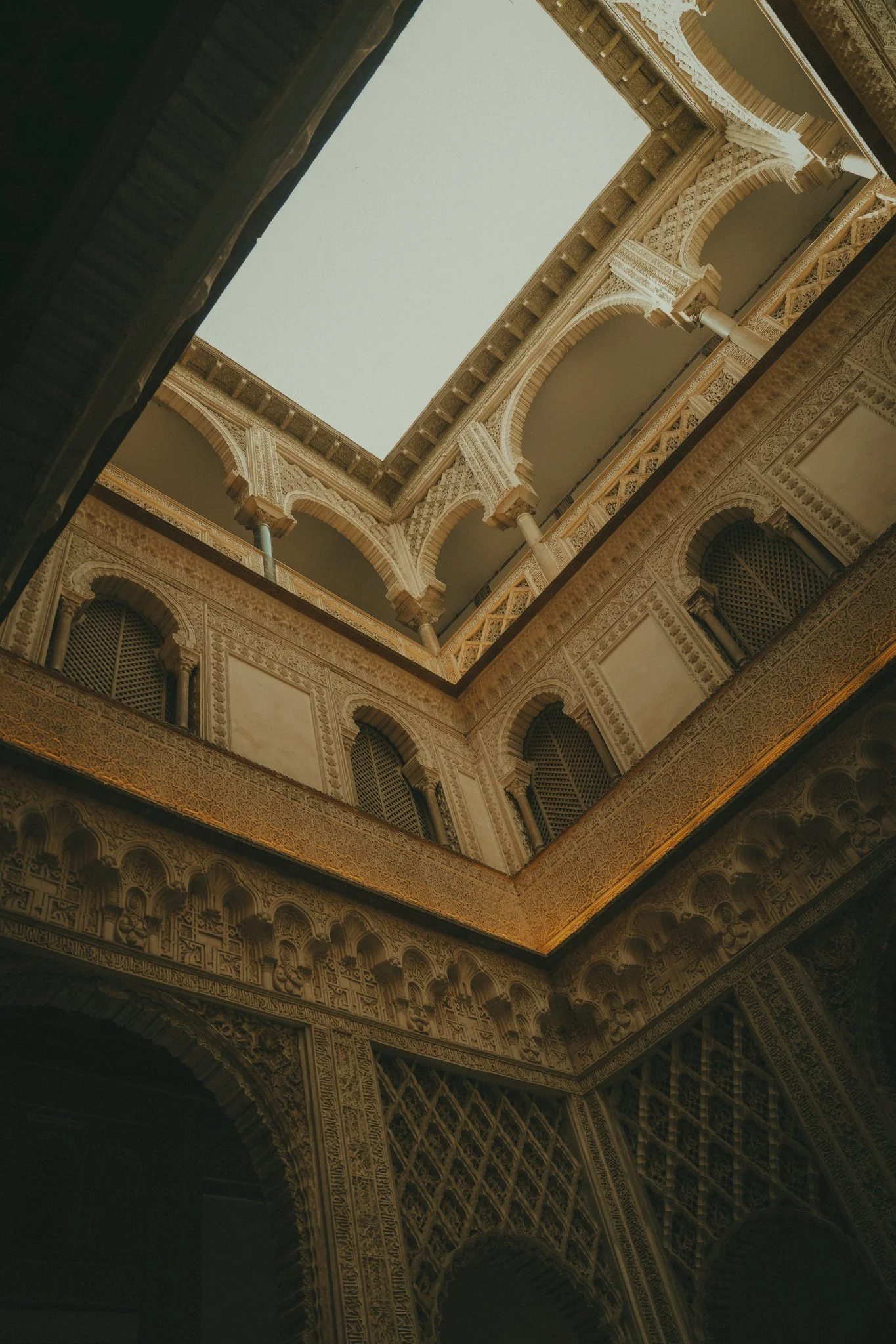 Intricately decorated interior courtyard with ornate arches, columns, and detailed carvings, viewed from below upward toward an open roof.