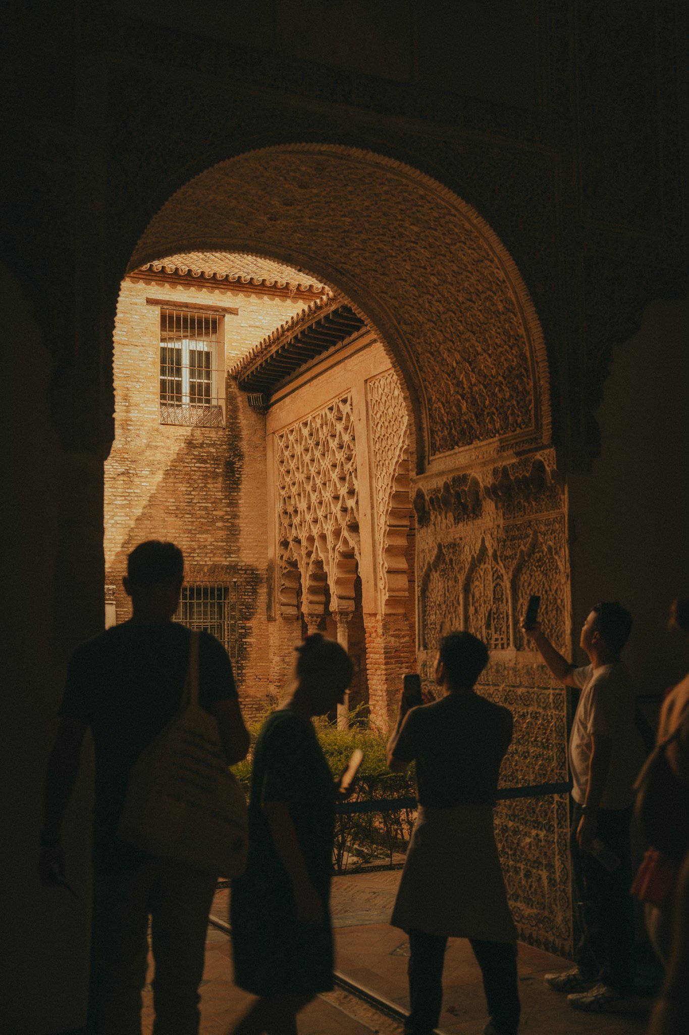 Group of people viewing intricate architectural details of a historic building at night, with arched doorways, decorative carving, and brick walls.