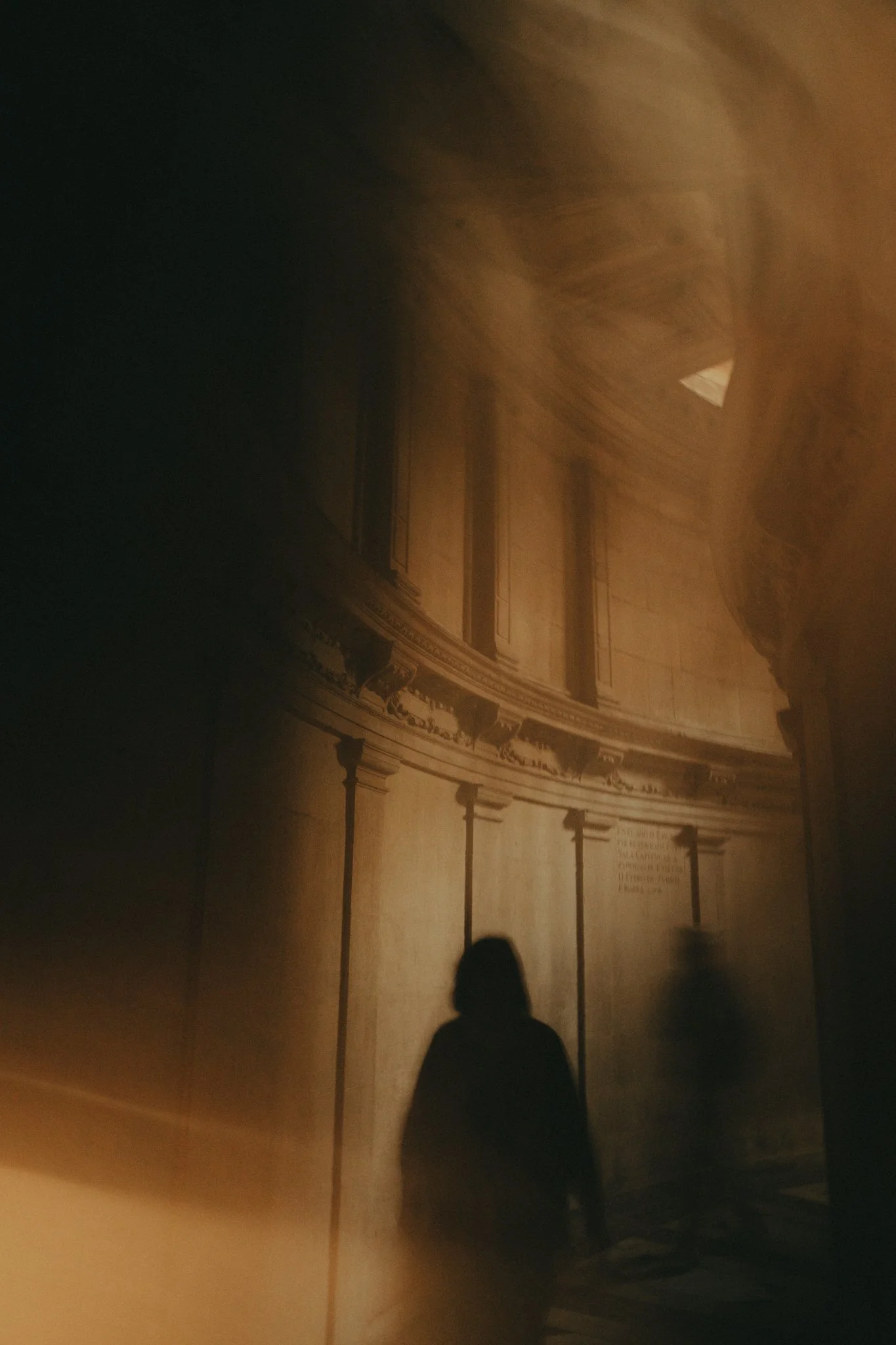 A person stands in front of a large, ornate wooden wall with gold accents and decorative molding, backlit by warm lighting.