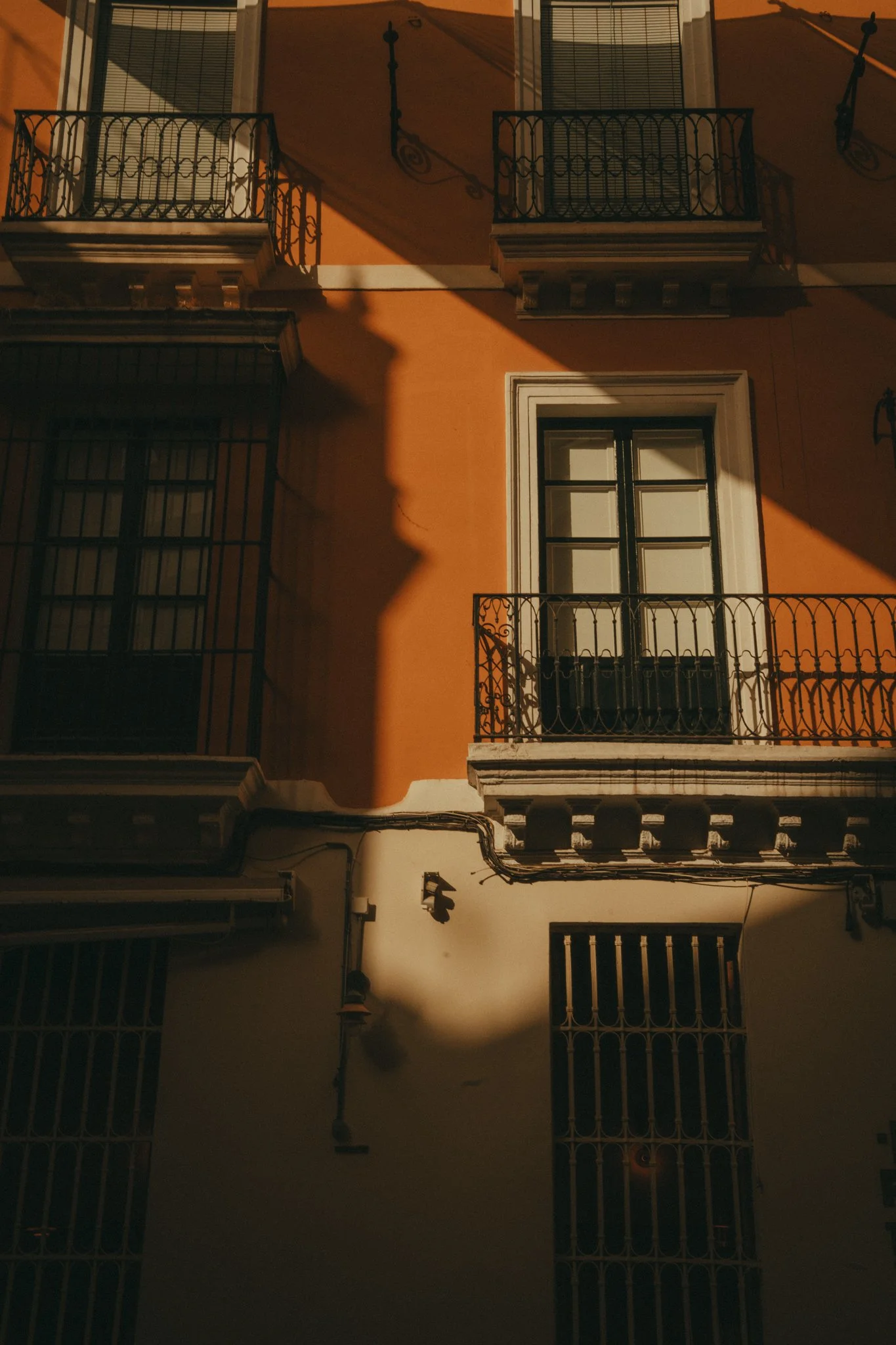 The photo shows the exterior of a building with multiple windows and balconies, with shadows cast across the wall, indicating it was taken in the late afternoon or early evening.