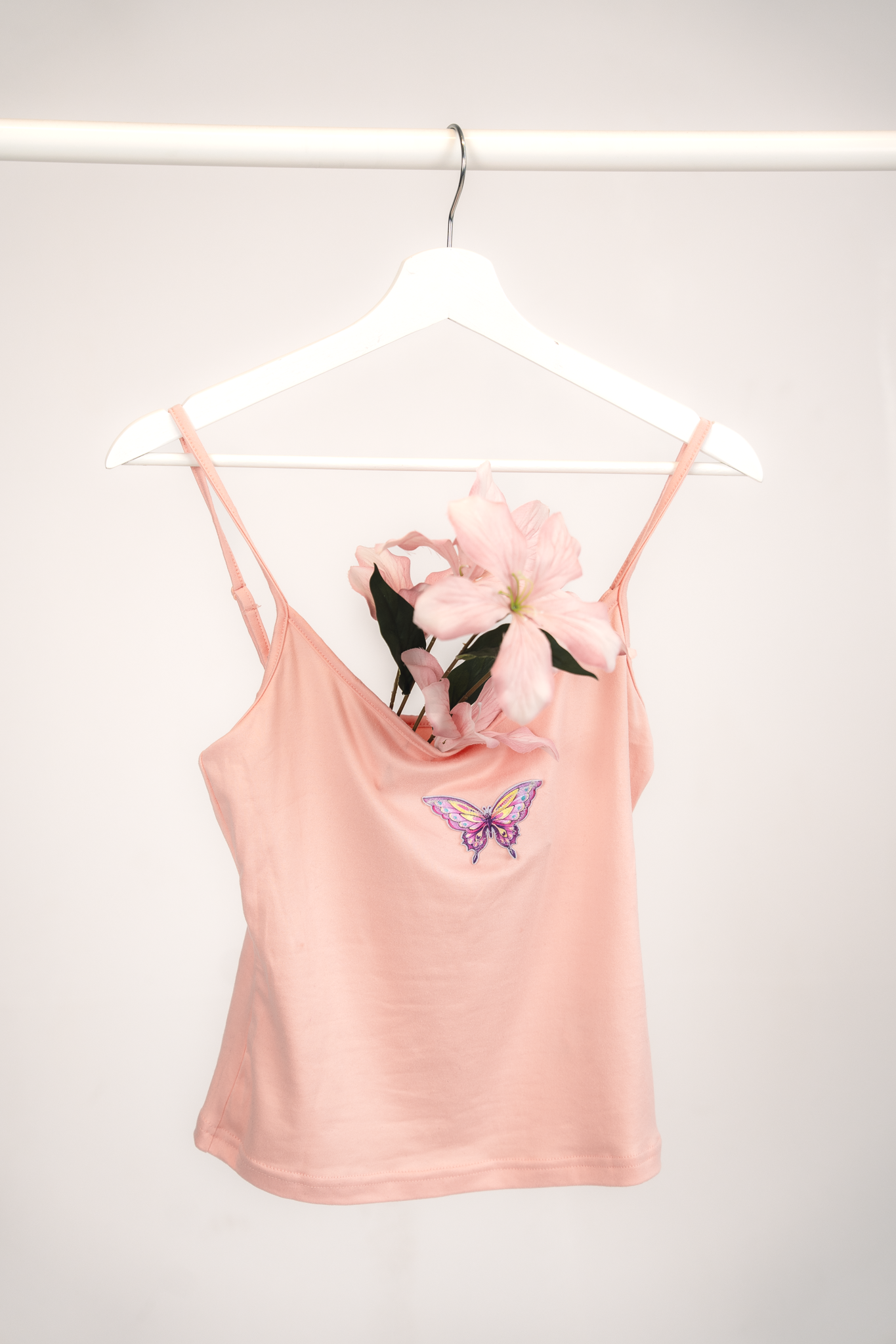 A pink dress with a butterfly patch hanging on a white hanger on a white rod.