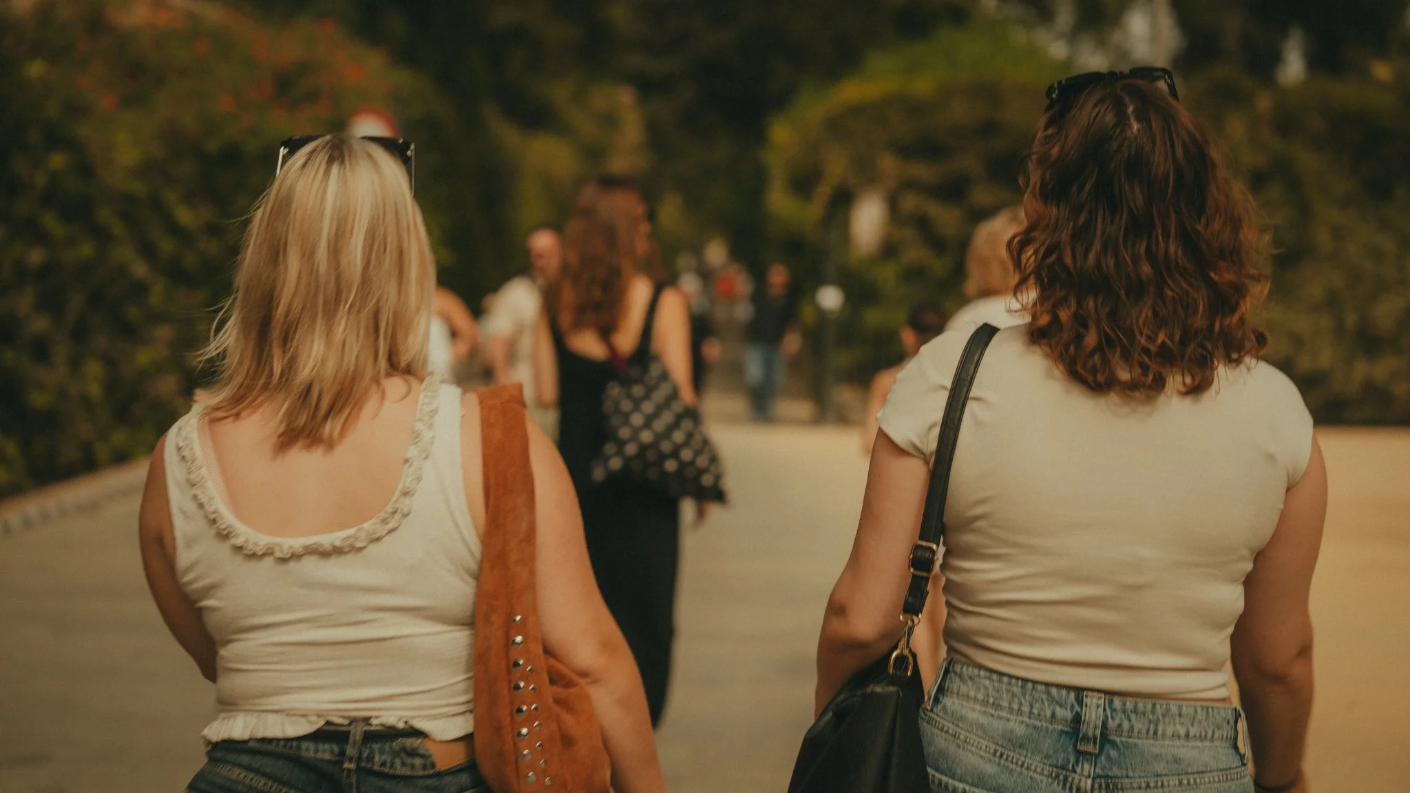 Two women walking outdoors at sunset, with trees and other people in the background.