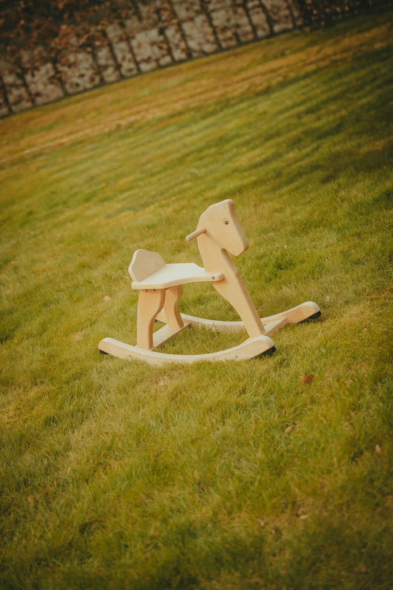 A wooden rocking horse on a grassy lawn, with a brick wall in the background.