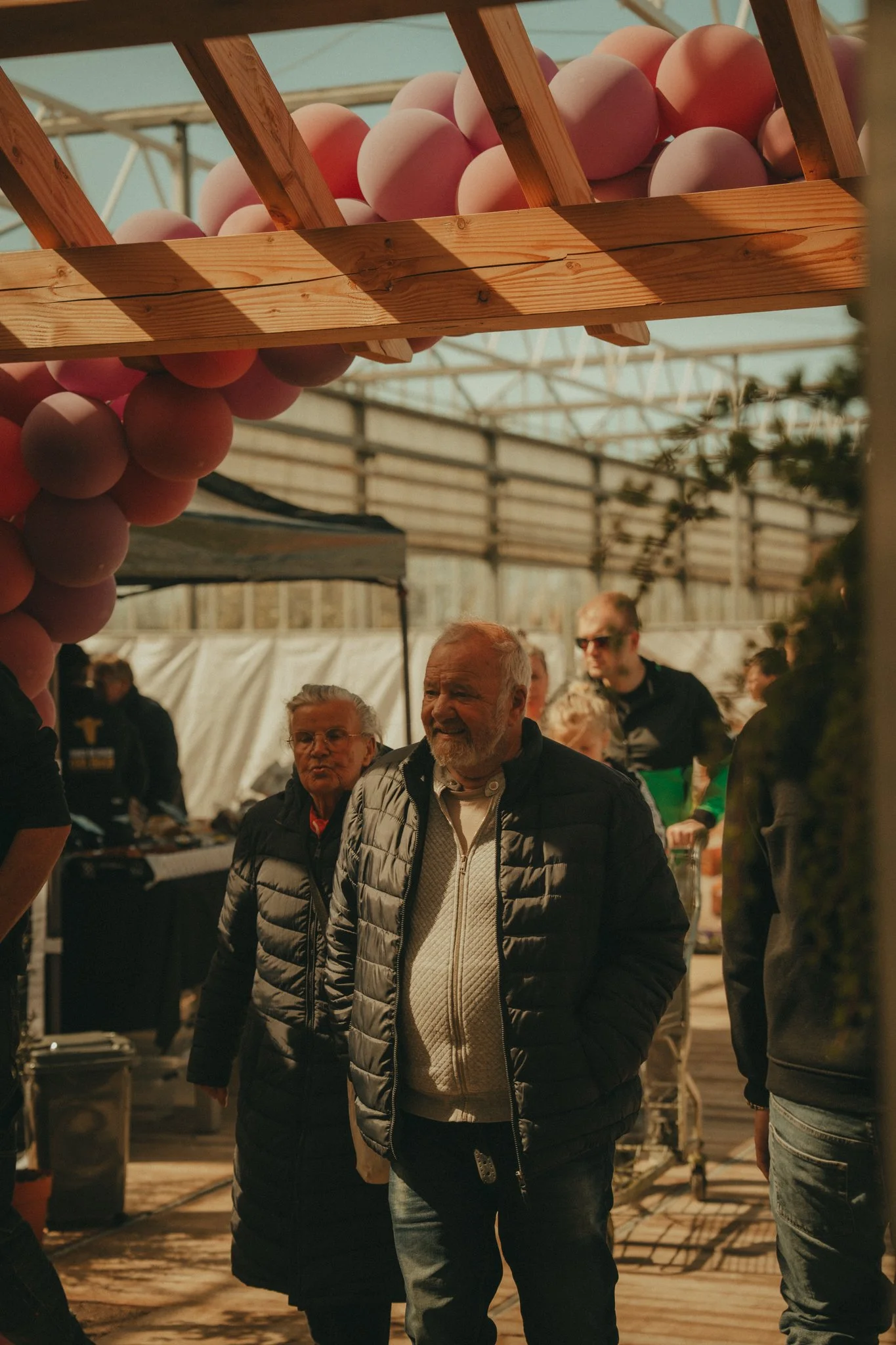 People shopping for eggs at an outdoor market, with eggs displayed in a wooden rack above them.