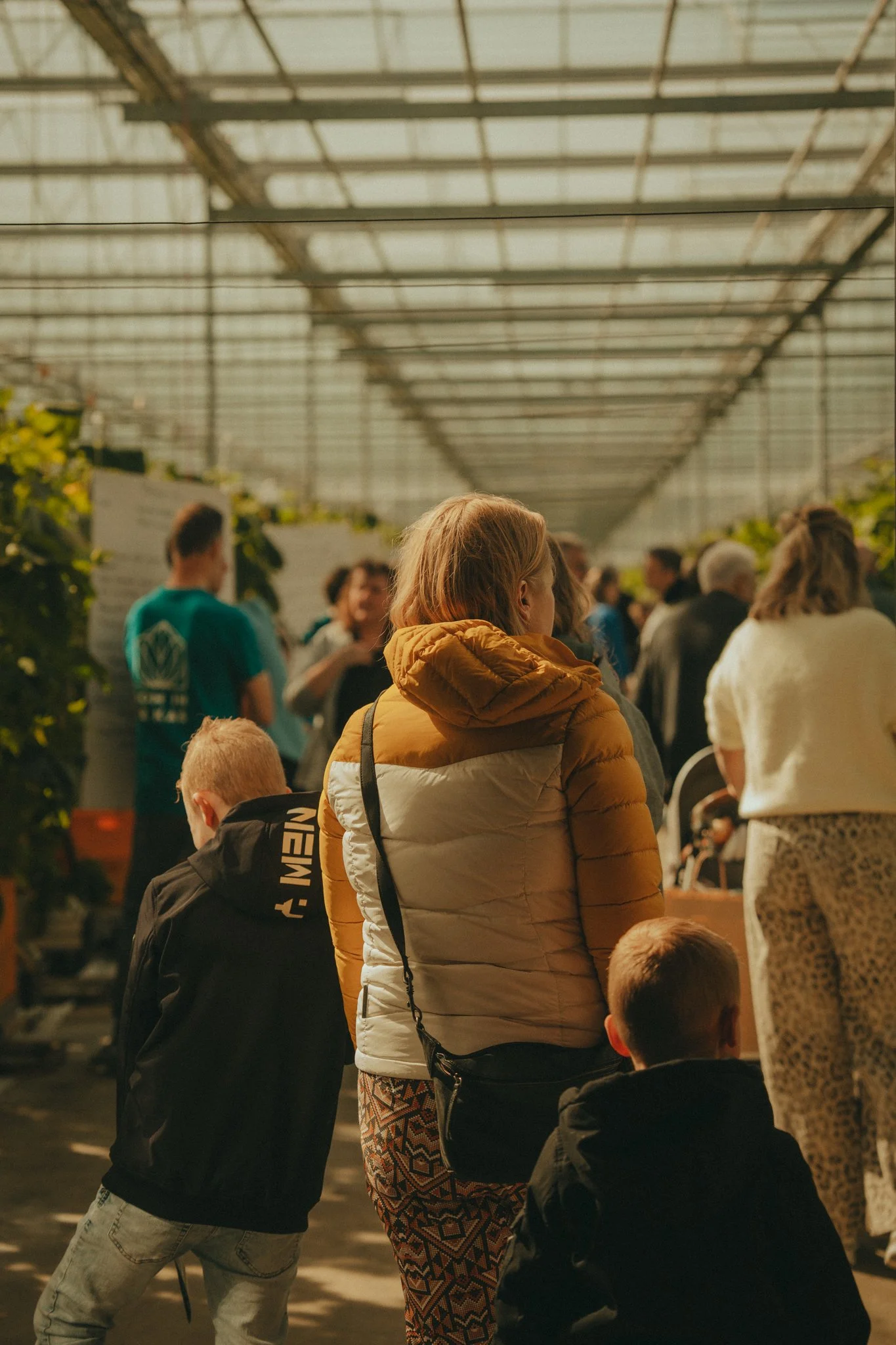 People standing in a greenhouse or indoor garden, some facing away, wearing casual clothing.