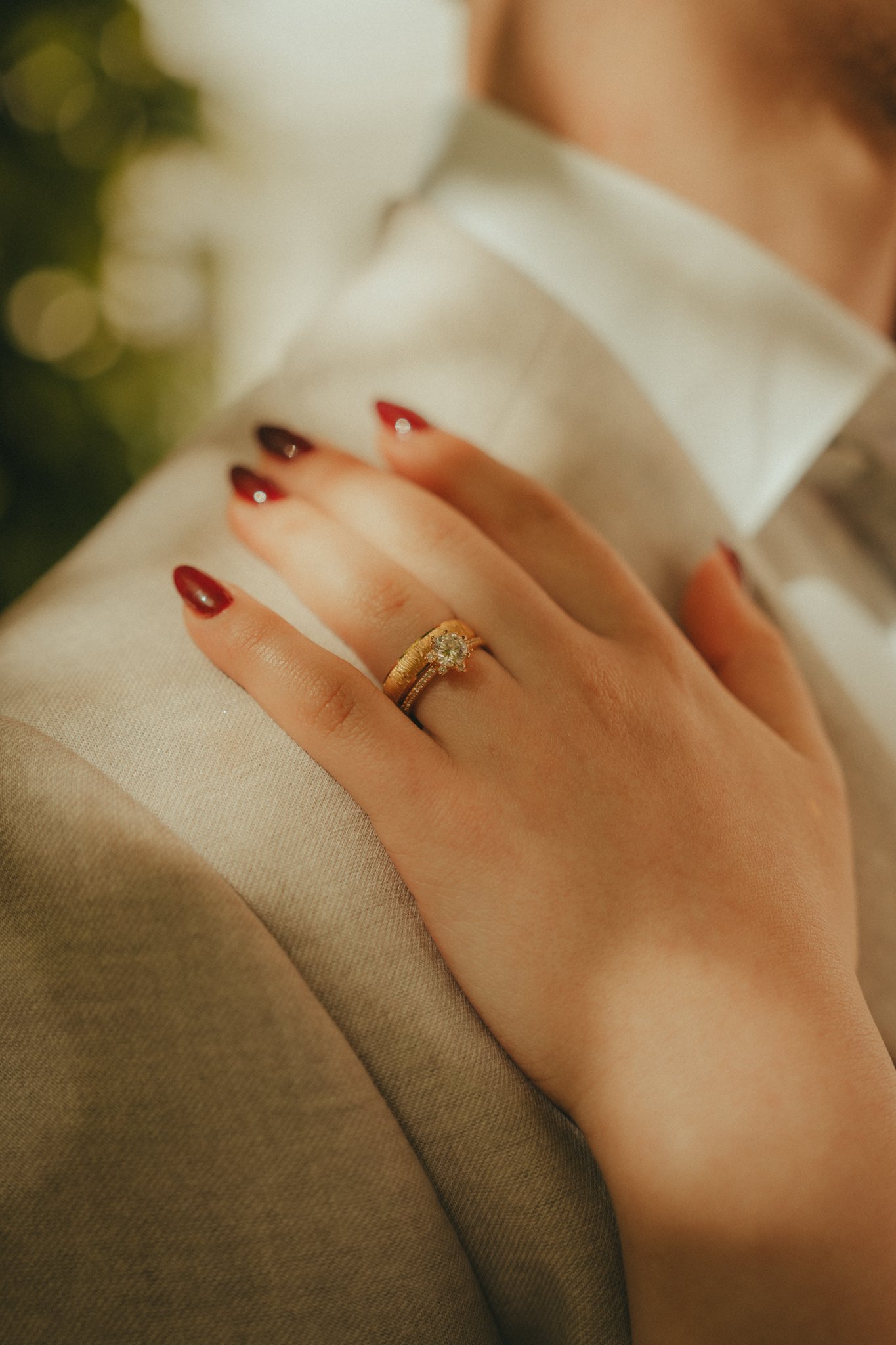 Close-up of a woman's hand showing a wedding ring with a diamond, resting on beige fabric.