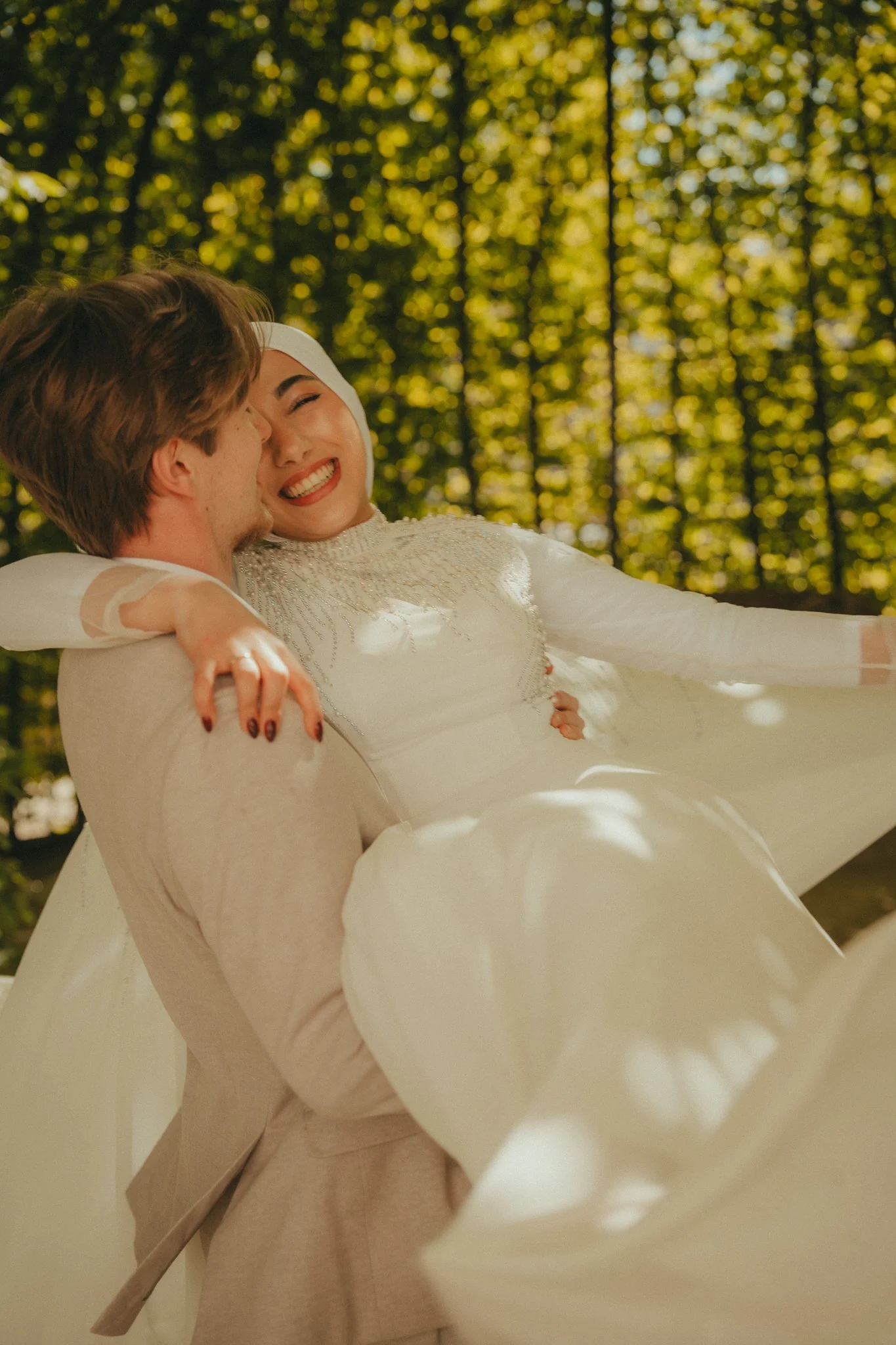 A couple is dancing together, with the woman smiling joyfully and the man holding her. Their faces are close, and they are in a bright, outdoor setting with trees and sunlight.
