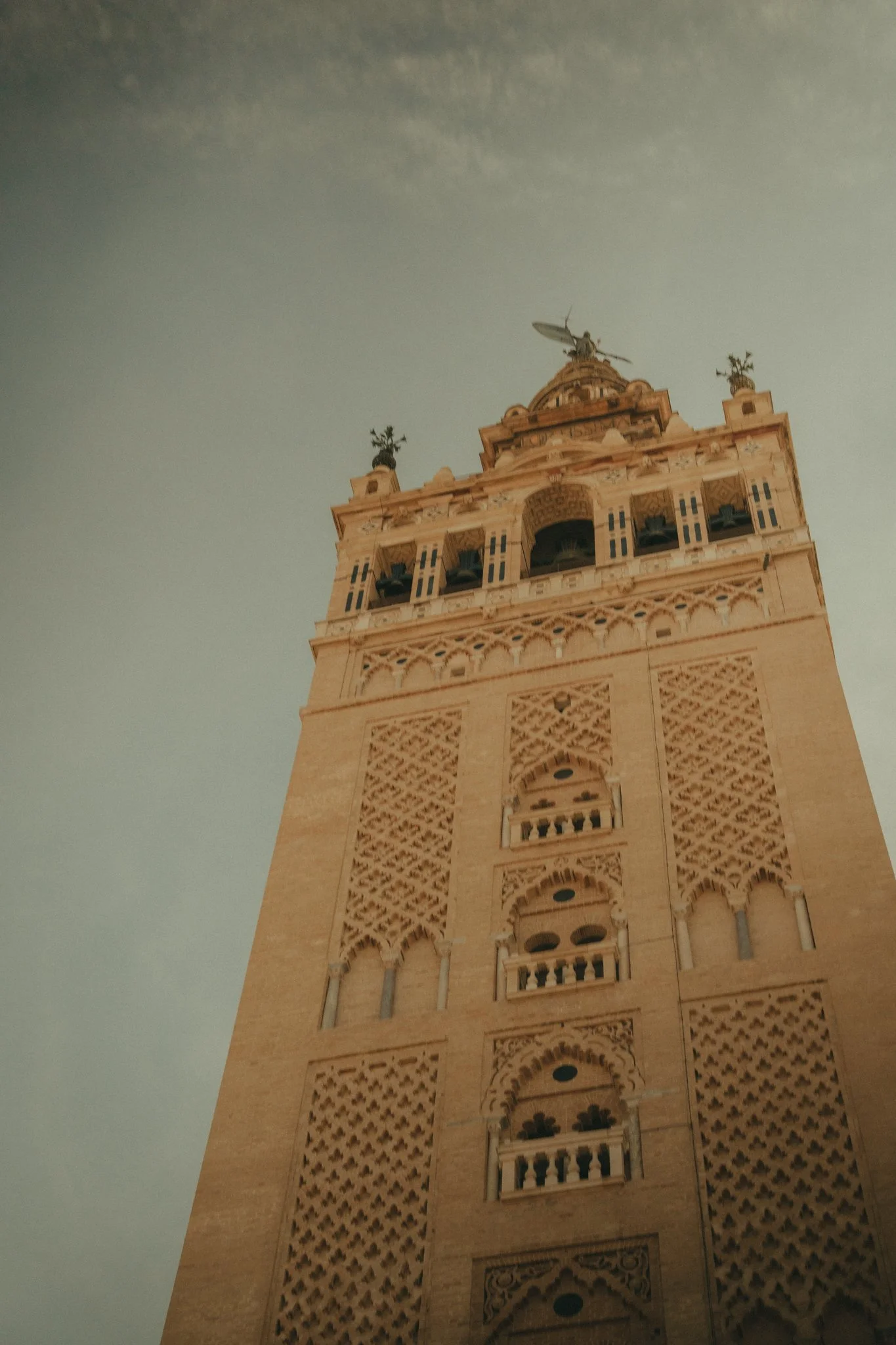Tall historic bell tower with intricate architectural designs and small balconies, topped with a drone.