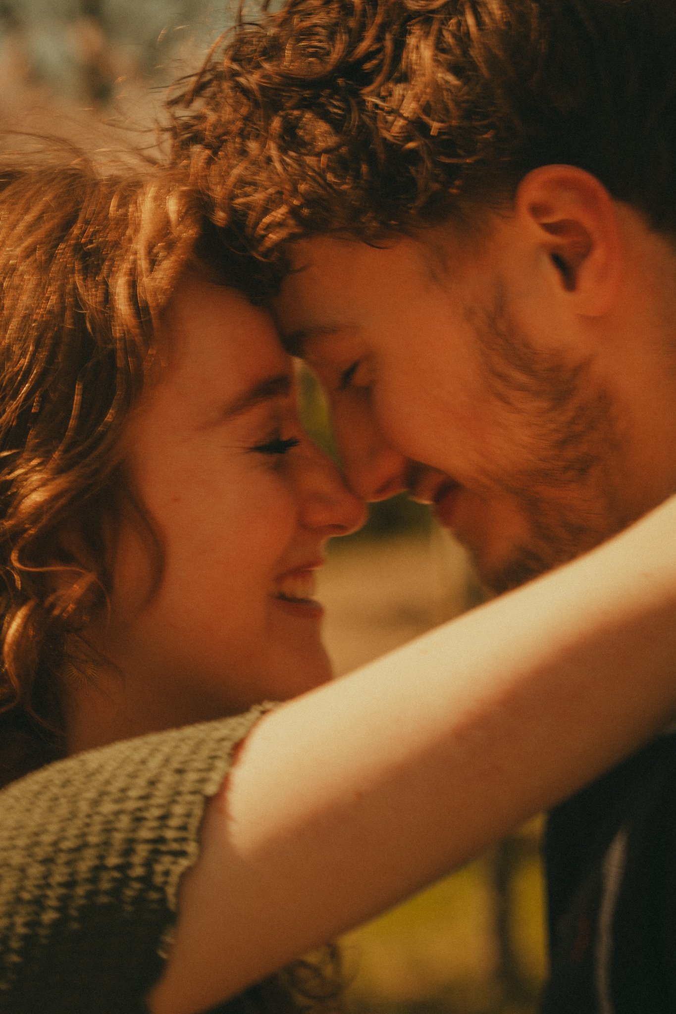 A close-up of a couple with their foreheads touching and eyes closed, sharing an intimate moment in warm lighting.